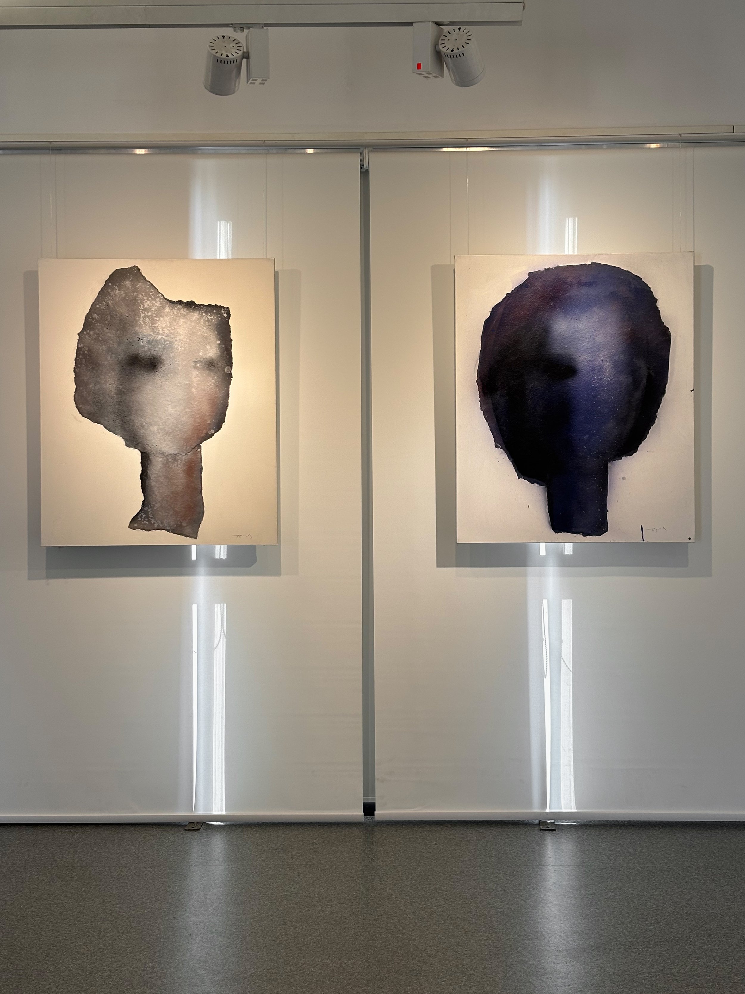Two abstract paintings of faces with dark and light tones displayed on a gallery wall.