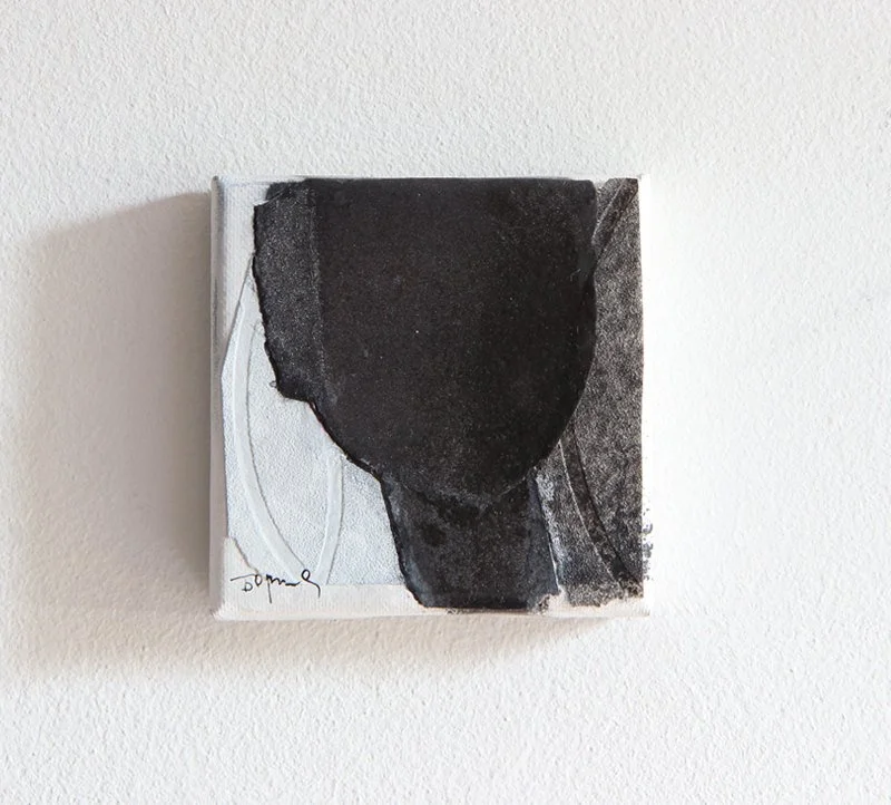 Small abstract painting with a black shape on a light gray background on a white wall.