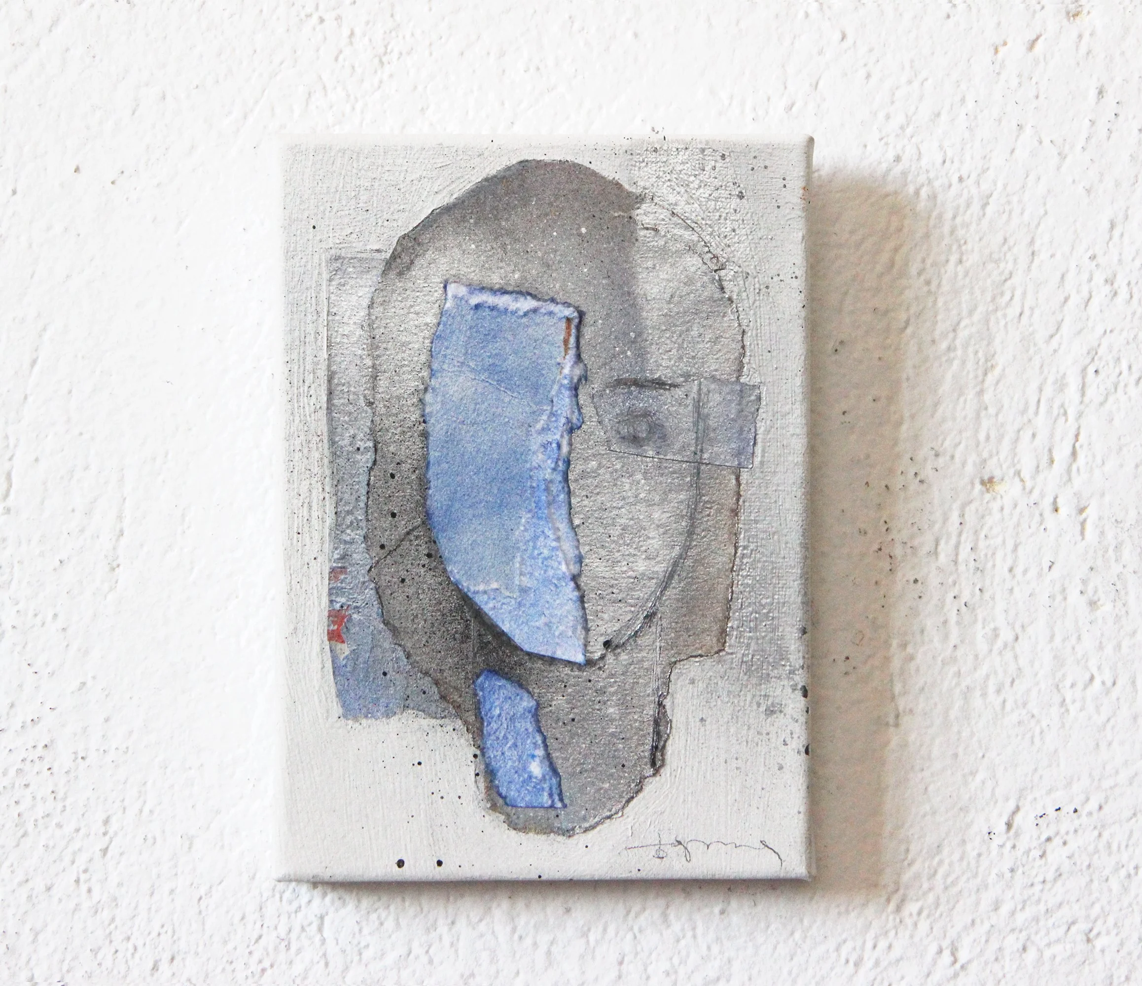 Mixed media abstract artwork featuring a gray and blue color palette on a textured canvas, mounted on a white wall.