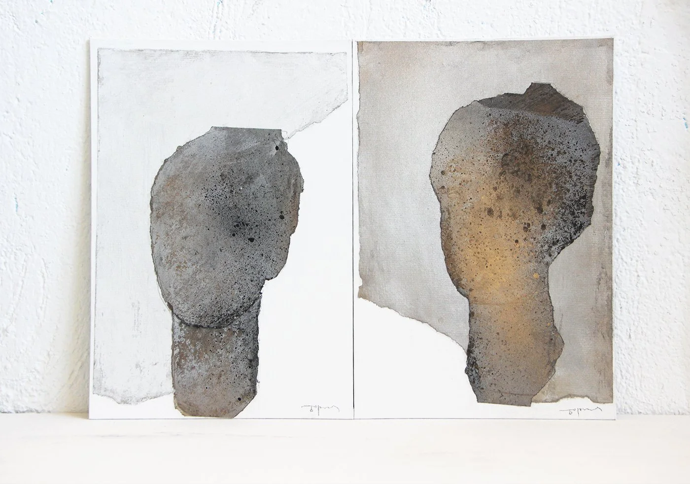 Two abstract paintings of human faces with textured, earthy tones, mounted on a white wall.