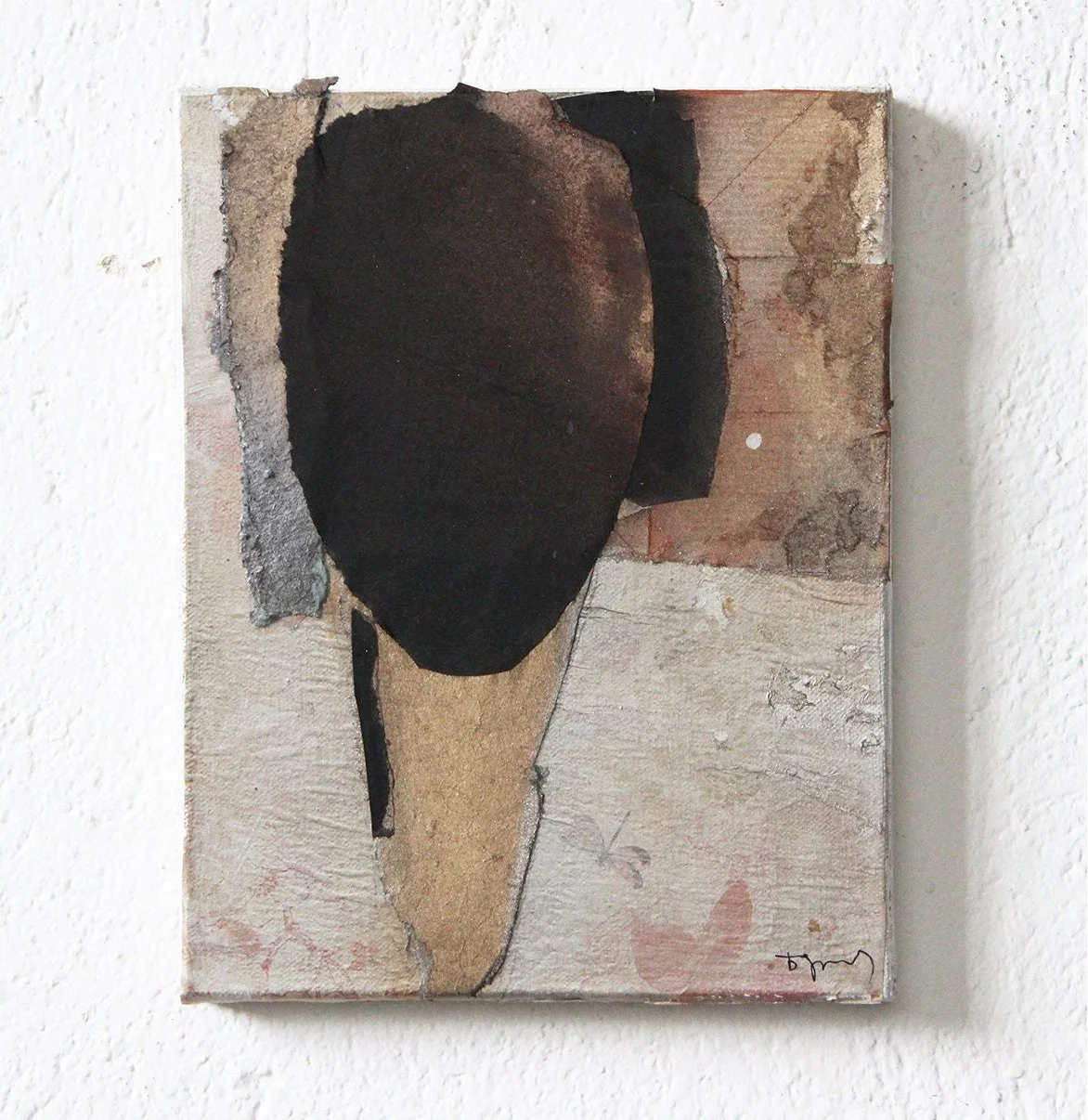 Abstract mixed media artwork featuring a black oval head shape with textured, earthy tones on a textured beige and brick background, mounted on a white wall.