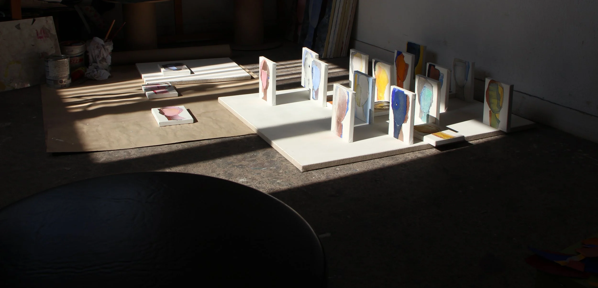 Colorful abstract artworks displayed on small stands and arranged on a table, illuminated by sunlight through a window.