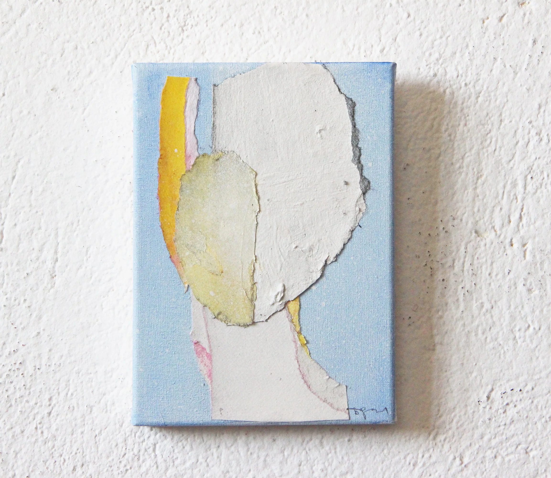 Abstract artwork of a woman with a large white face, yellow hair, and a blue background, painted on a small canvas hung on a textured white wall.