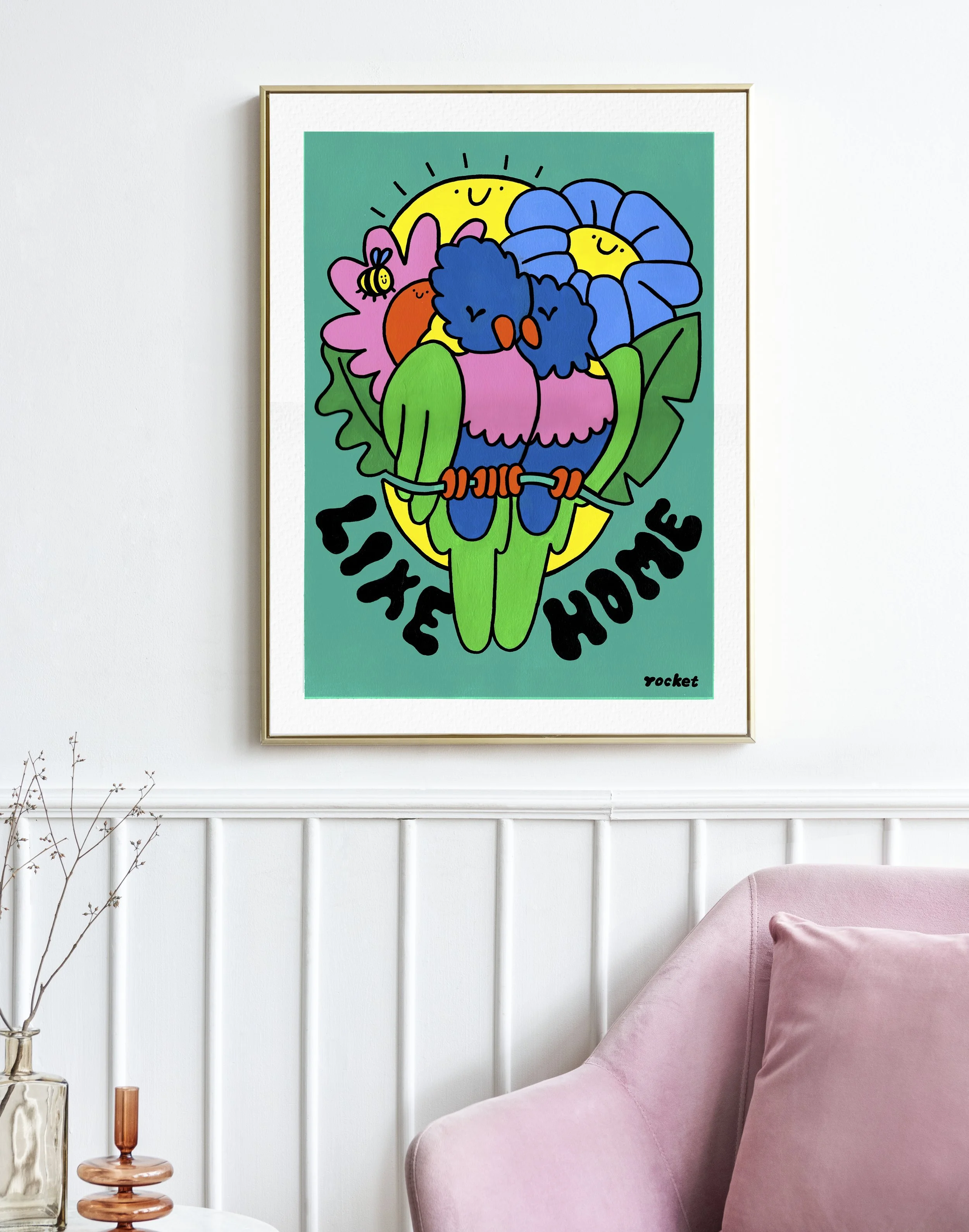 Illustration in einem Rahmen an der Wand hängend von zwei Regenbogenloris mit Blumen und einer Sonne im Hintergrund und Schrift: Like Home.