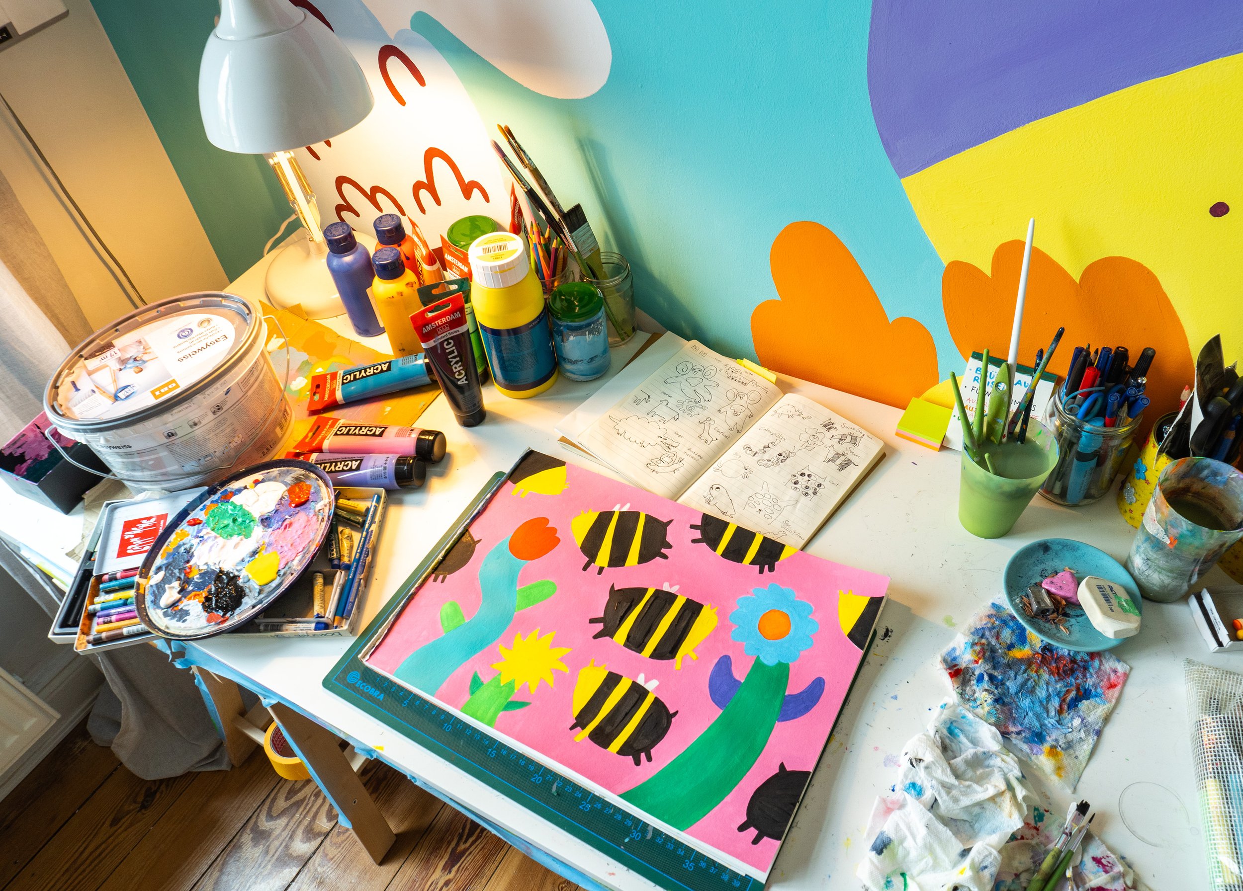 Arbeitsplatz einer Künstlerin. Der Schreibtisch ist voll mit Farben, Stiften und Pinseln. Prozess einer Illustration.
