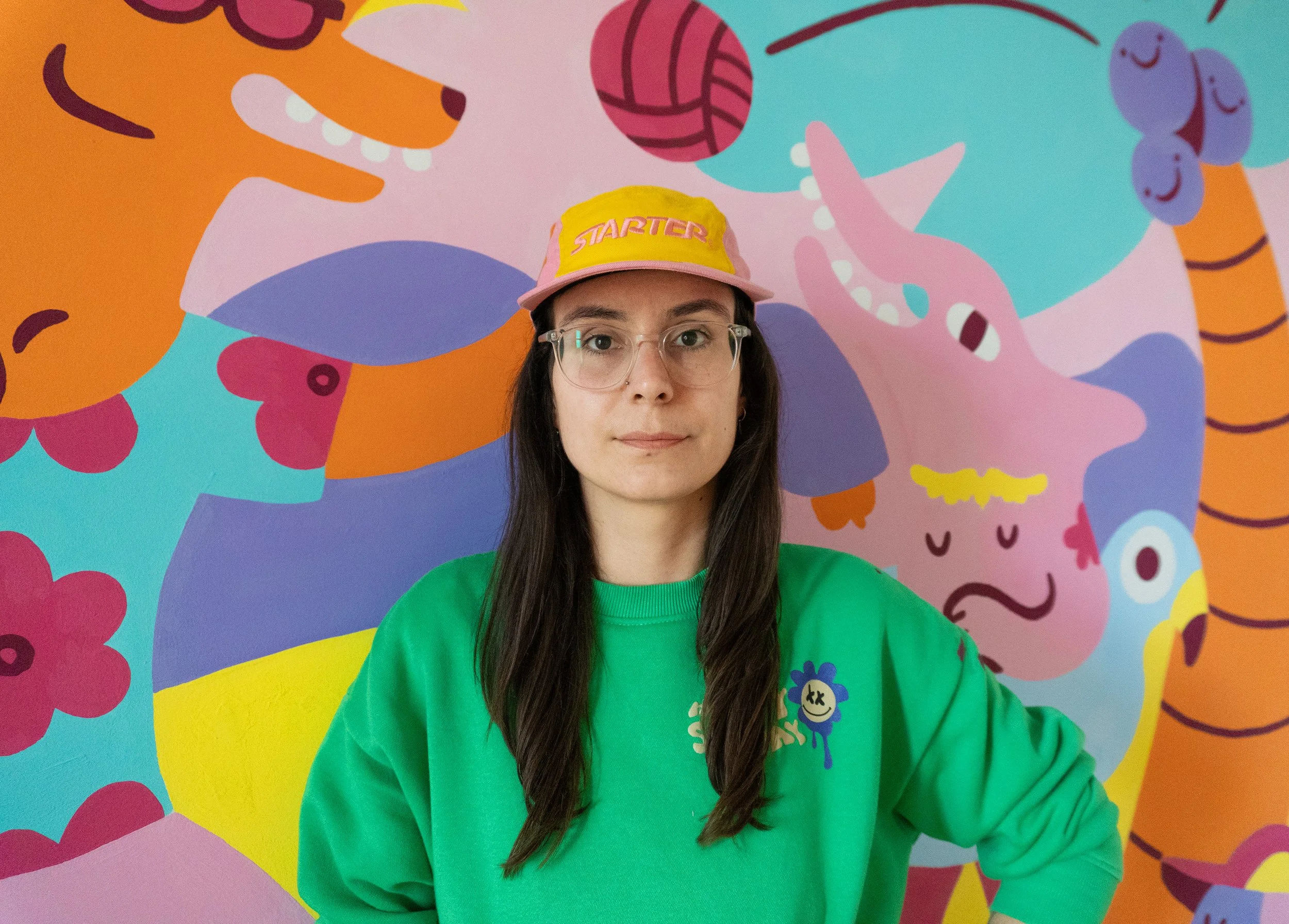 Junge Frau trägt pinke Cap vor einem bunten Wandbild mit Tieren.