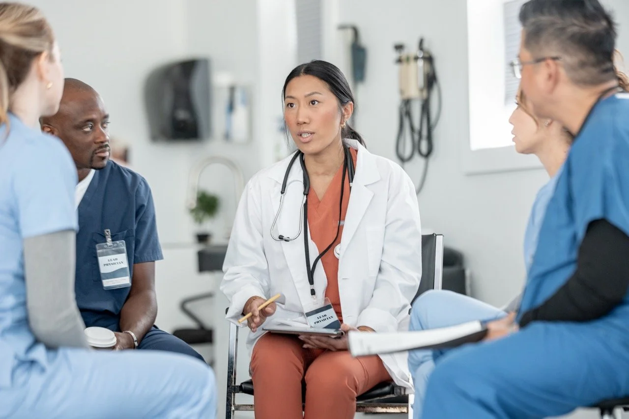 Medical team meeting with a female doctor speaking to colleagues in a hospital room.