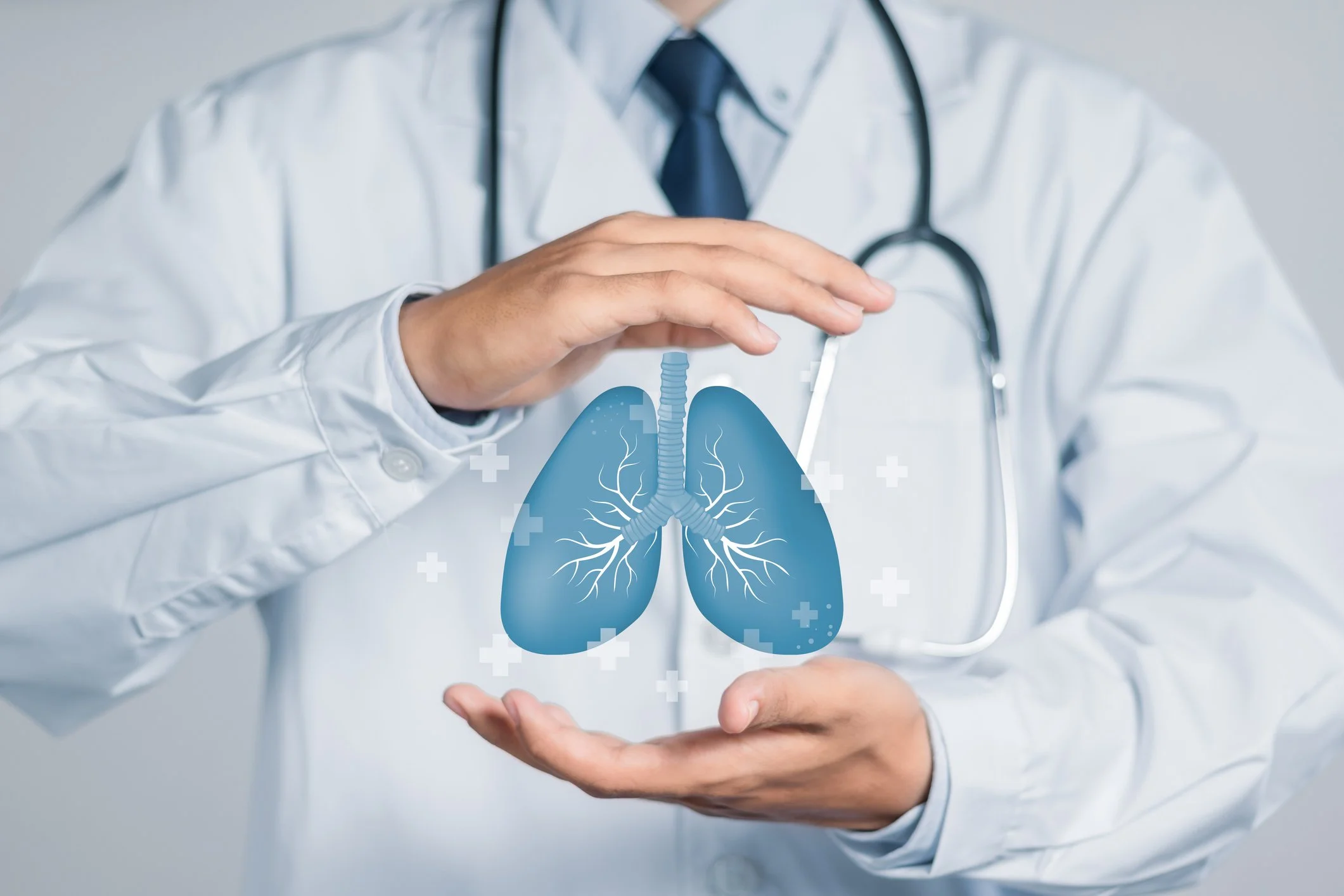 A doctor in a white coat with a stethoscope around his neck, holding and pointing to a transparent digital illustration of human lungs.