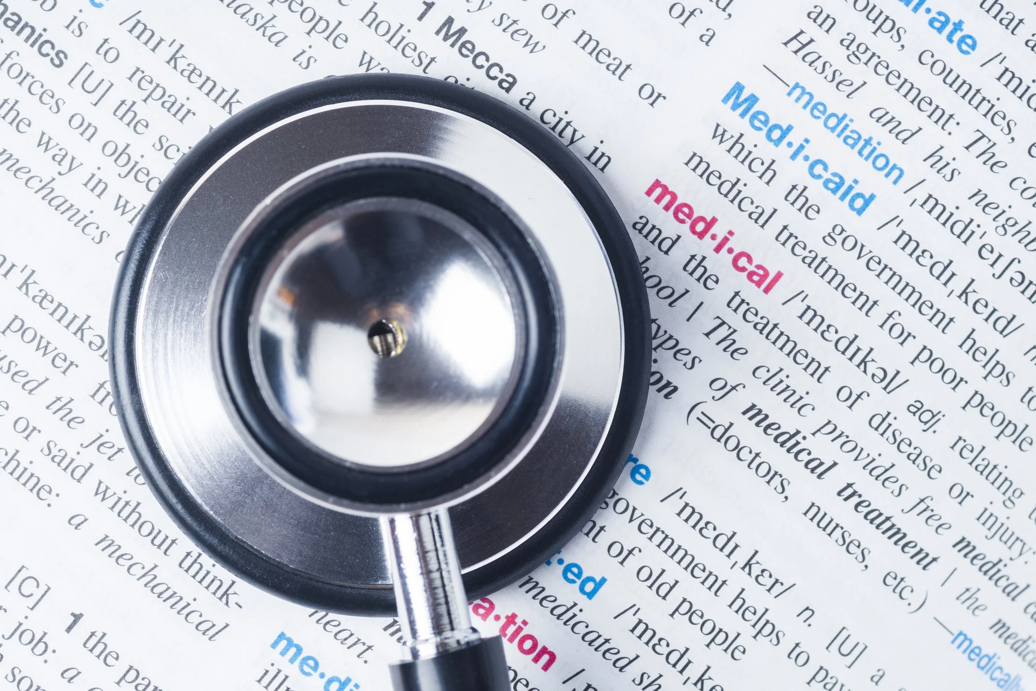 A stethoscope placed on top of a newspaper article with the words 'med:ical' and 'med:ication' highlighted in pink and blue.