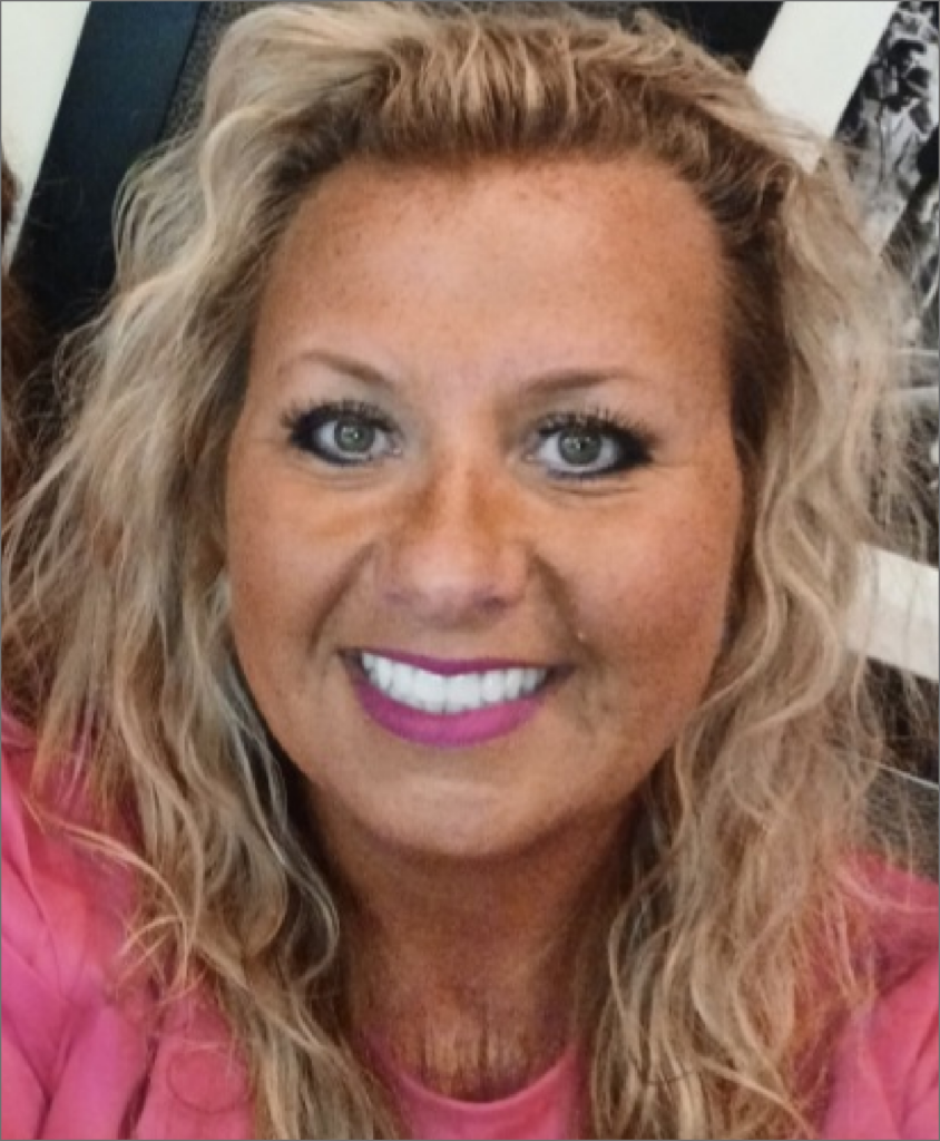 Close-up of a woman with curly blonde hair, blue eyes, wearing pink lipstick and a pink top, smiling.