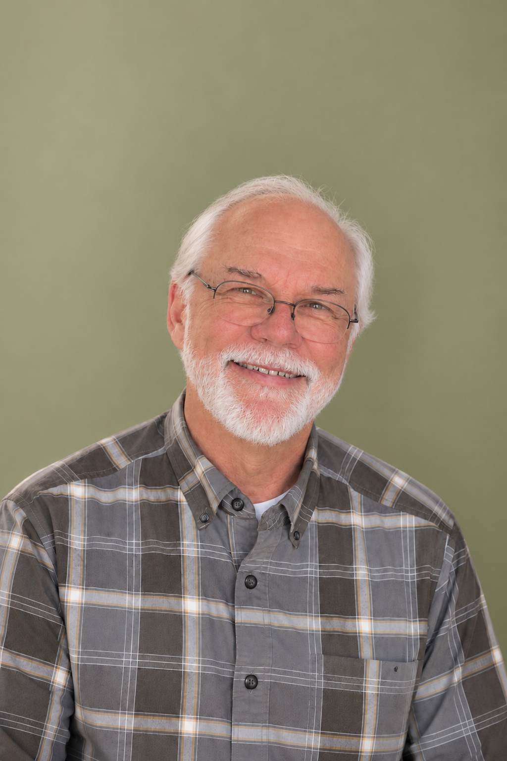 A man with white hair and a beard, wearing glasses and a plaid shirt, smiling at the camera against a light green background.