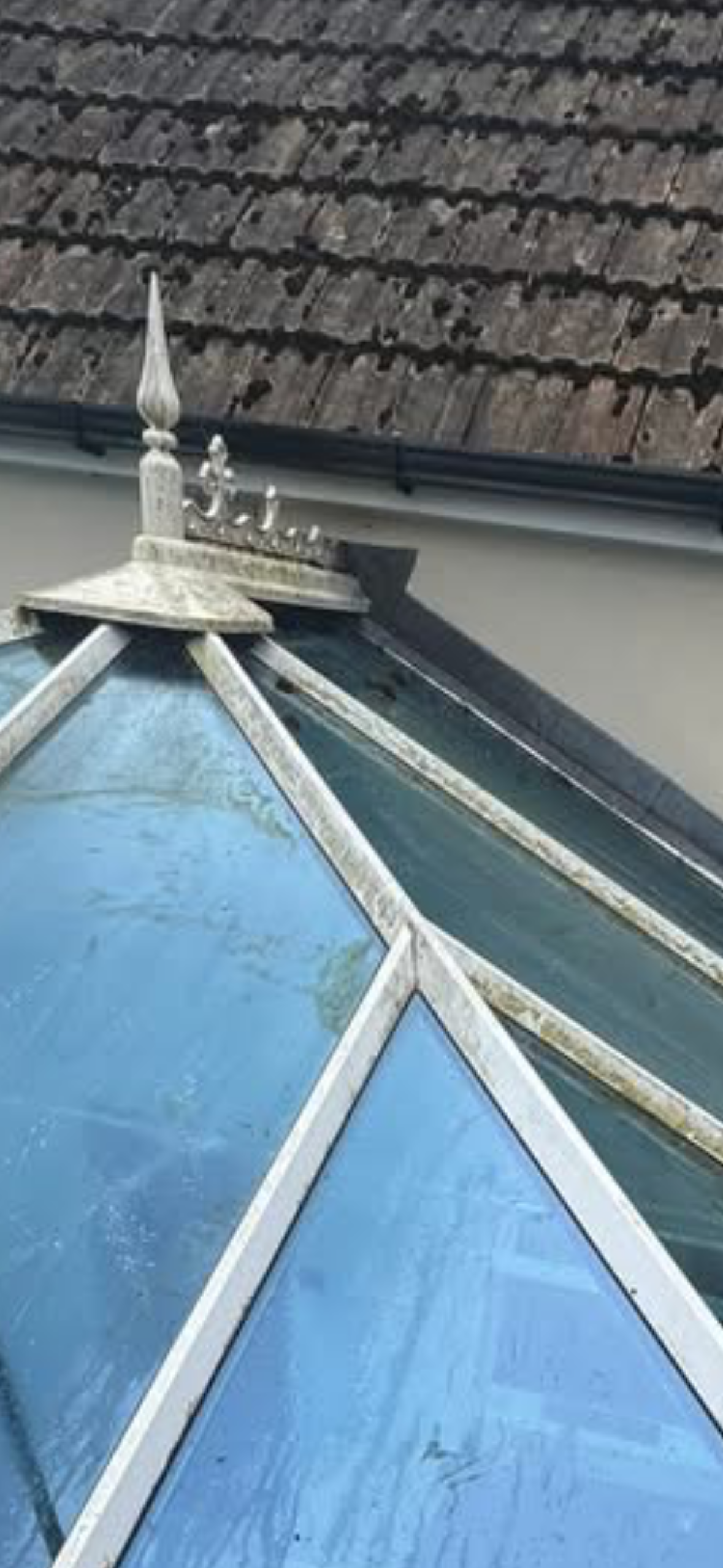 Close-up of a house roof with weathered, brown tiles and a glass roof with a metal frame, featuring a decorative metal ornament.