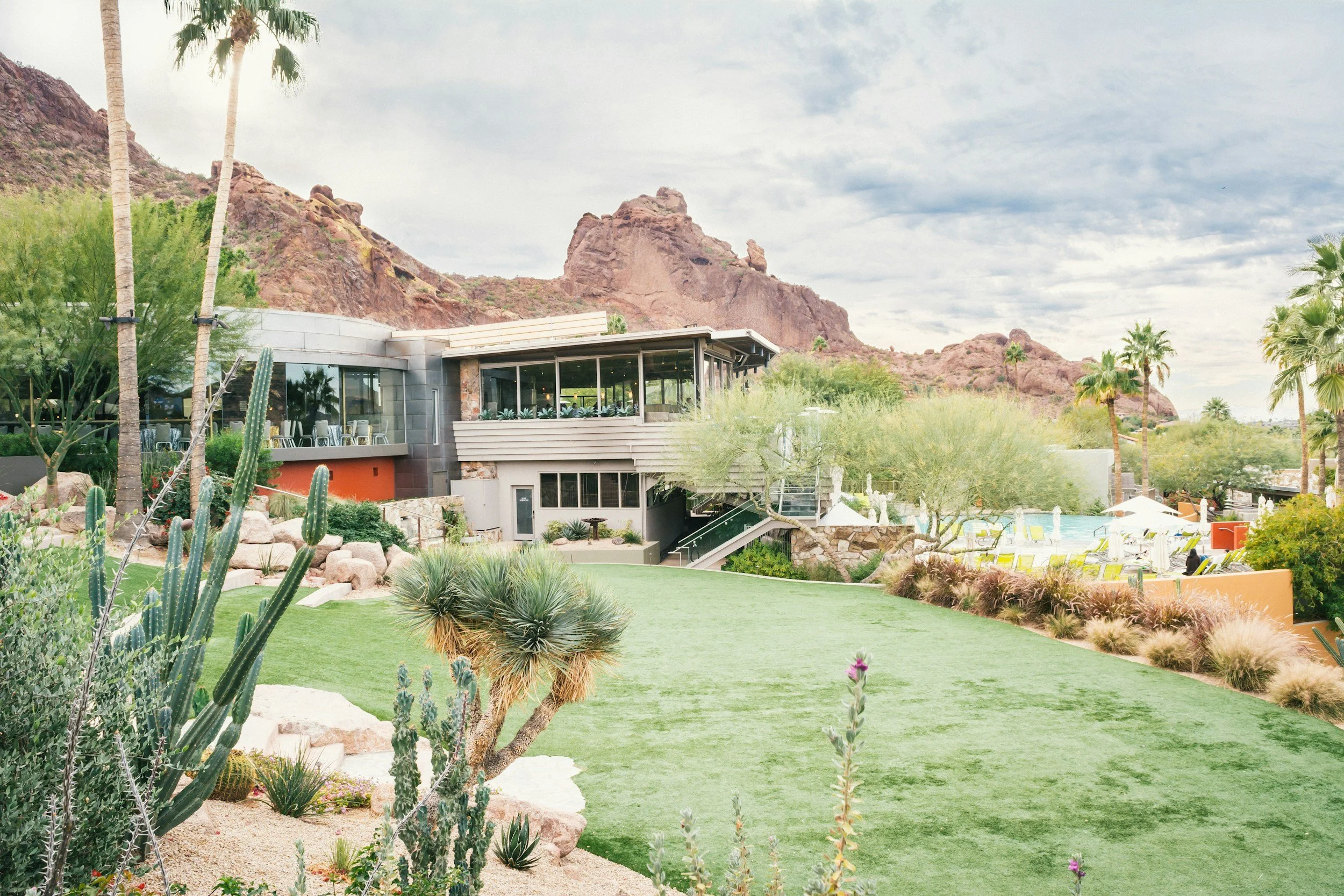 A modern building with large glass windows surrounded by desert landscaping and mountains.