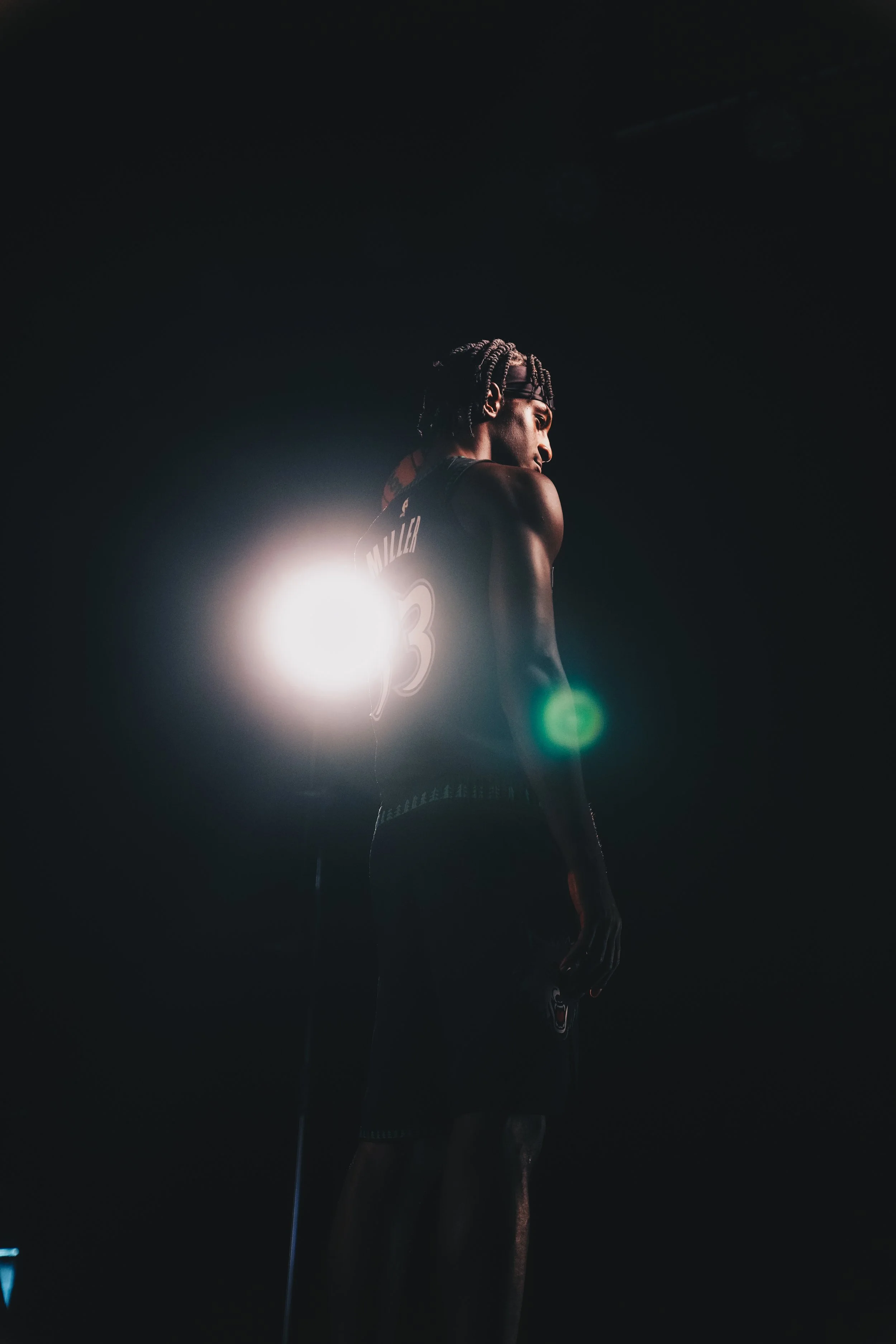 A basketball player stands in a dark room with a bright light behind them, creating a silhouette effect.