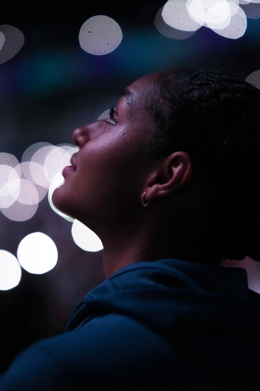 Side profile of a young woman with short hair looking upward against a background of blurred city lights at night.