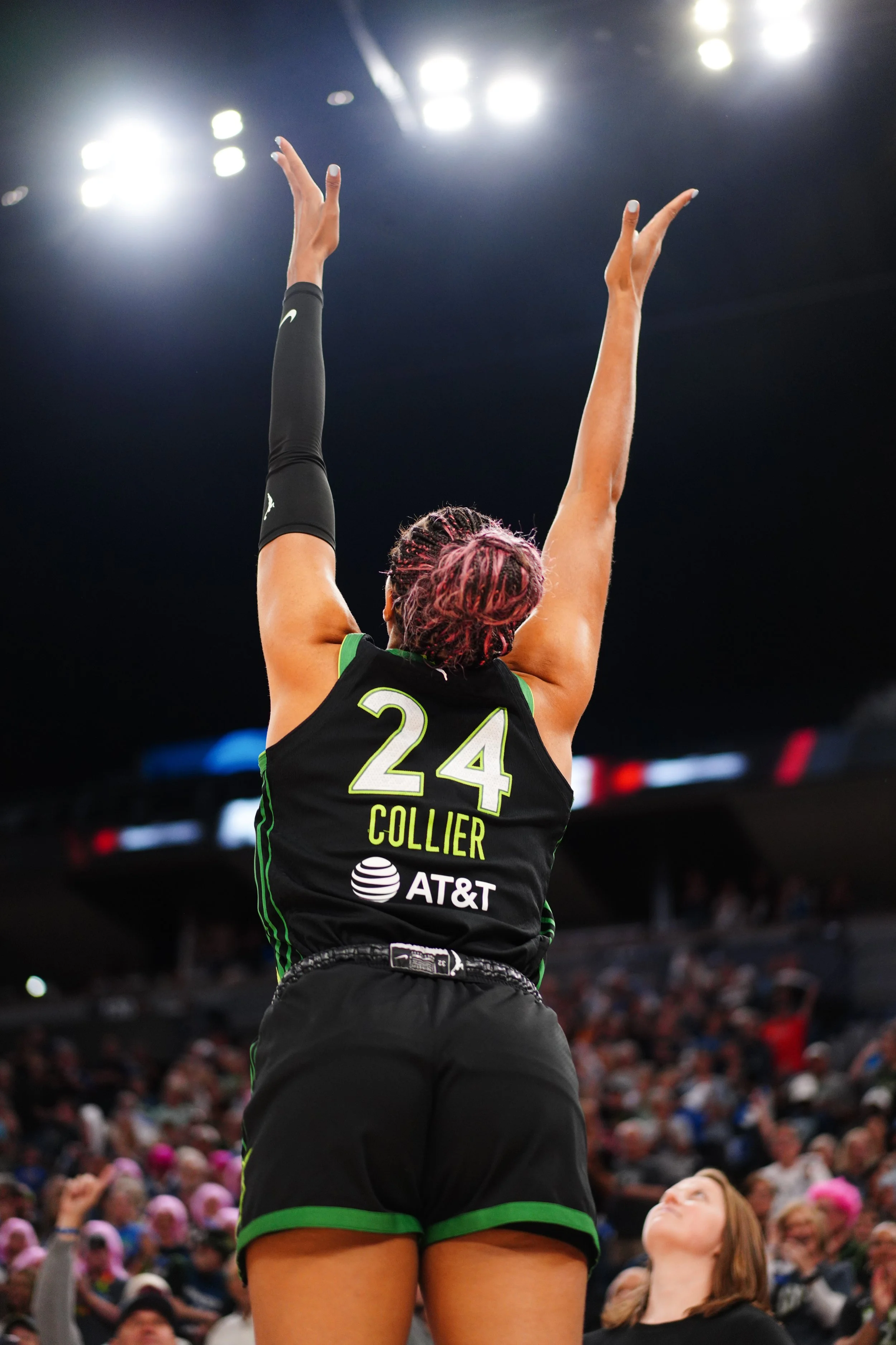 A female basketball player wearing a black and green uniform with the number 24 and the name Collier, in a basketball arena, preparing to catch or block the ball.