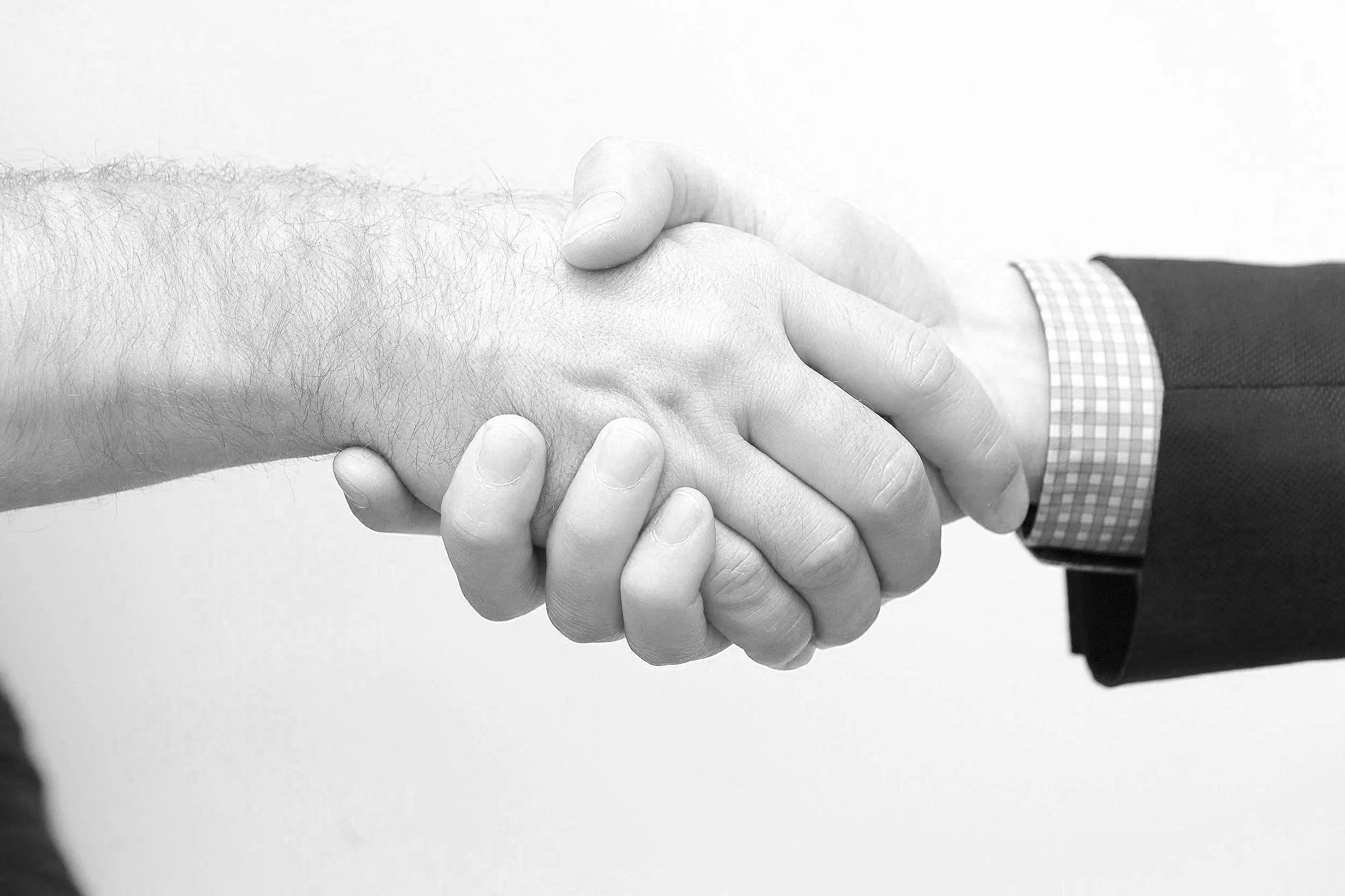 Close-up of a handshake between two people, one wearing a business suit with a checkered shirt. The image is in black and white.
