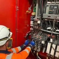 Technician wearing safety gear working on electrical equipment inside a control panel.