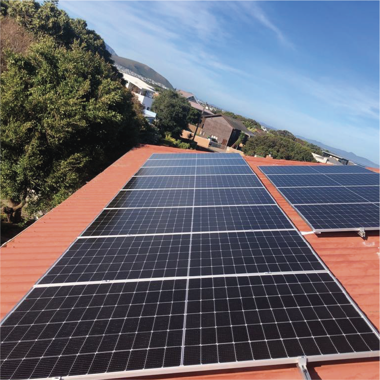 Solar panels installed on a rooftop with trees and buildings in the background under a blue sky.