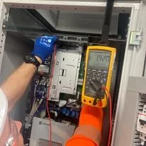 Technician using a multimeter to test an electrical circuit inside an electrical panel
