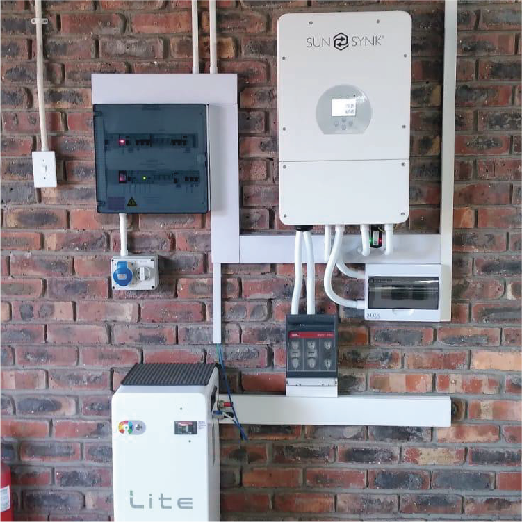 A solar power system installation on a brick wall, including a Sun Synk inverter, a white control box, a black combiner box, and various electrical connections and panels.