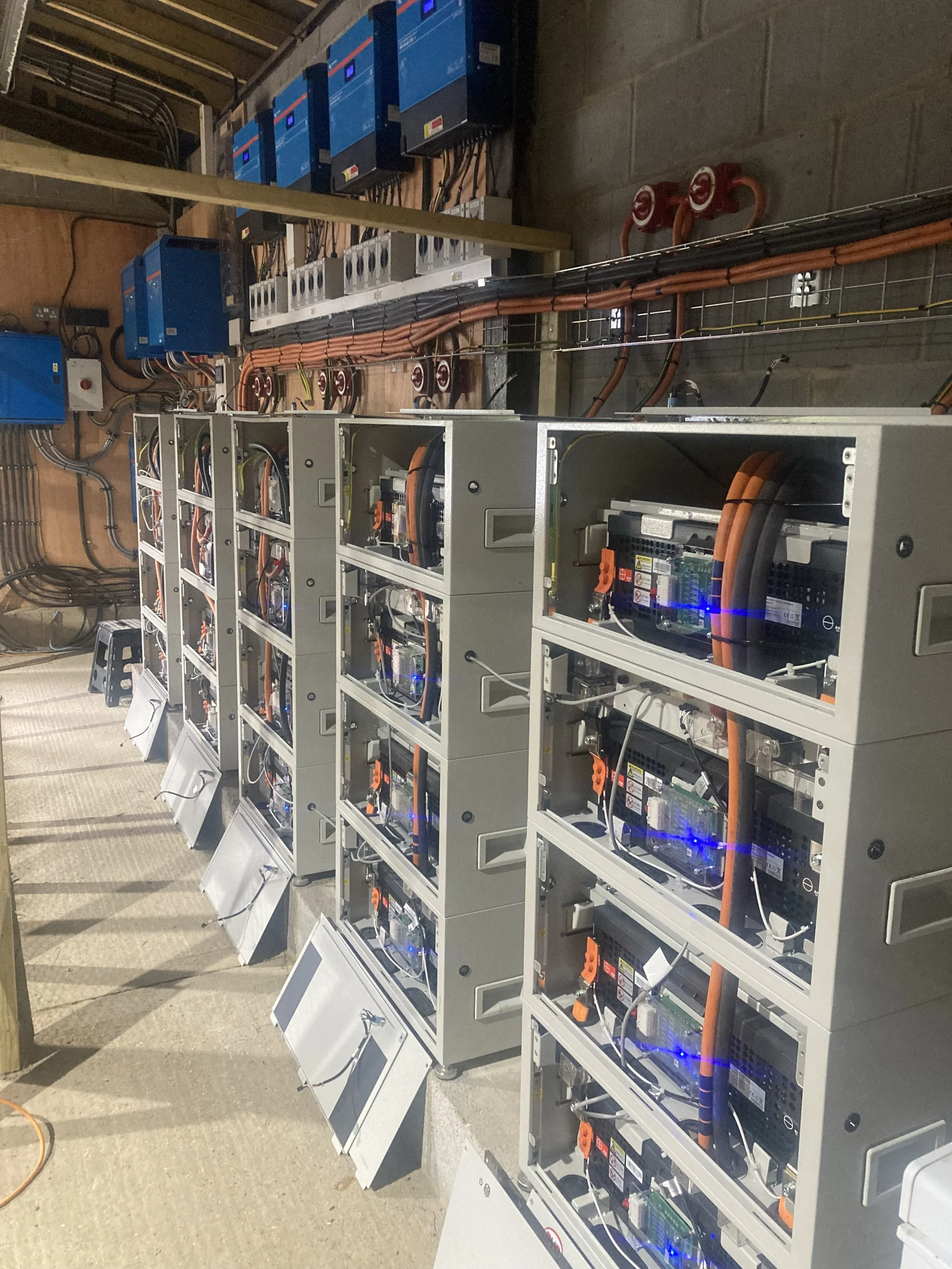 Row of electrical inverter units and cabinets with visible wiring and circuit boards in an industrial or data center setting.