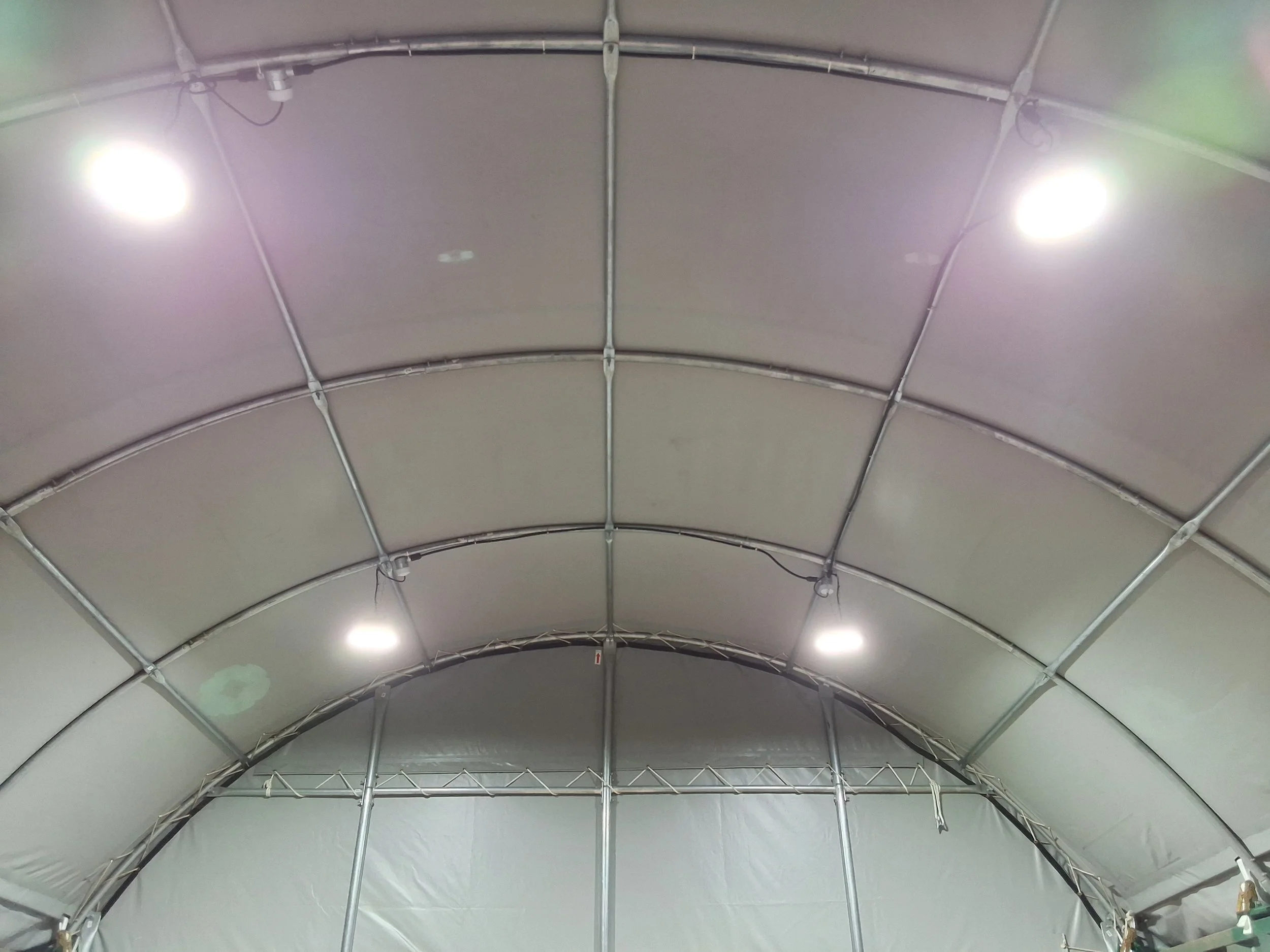 Inside view of a large tent structure with metal framework and bright lights on the ceiling.