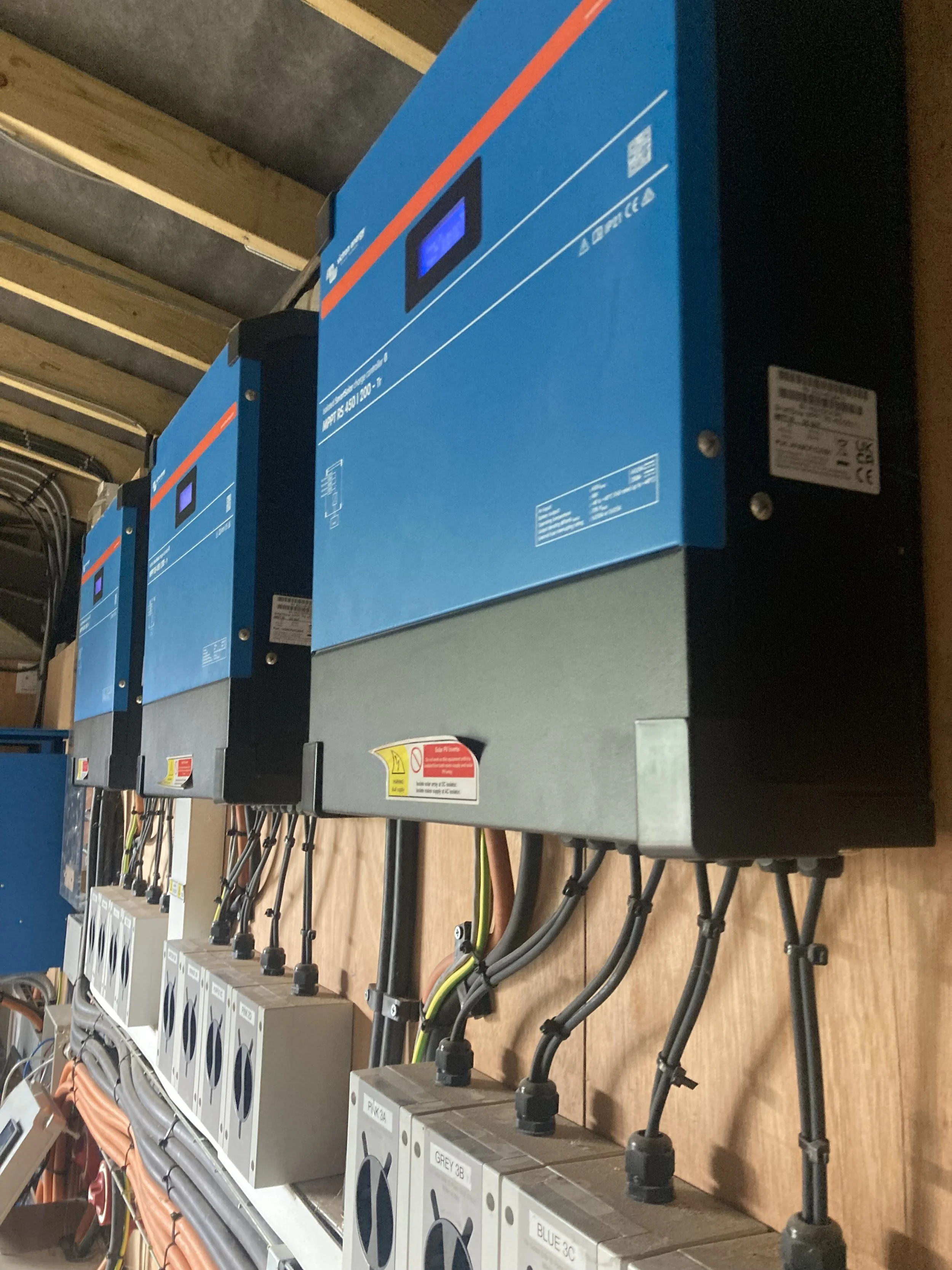 Electrical inverters mounted on a wooden shelf, with several power cables connected, in a technical or electrical setup.