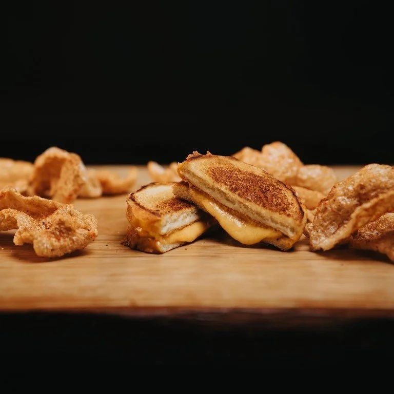 Close-up of toasted grilled cheese pieces on a wooden board against a black background.