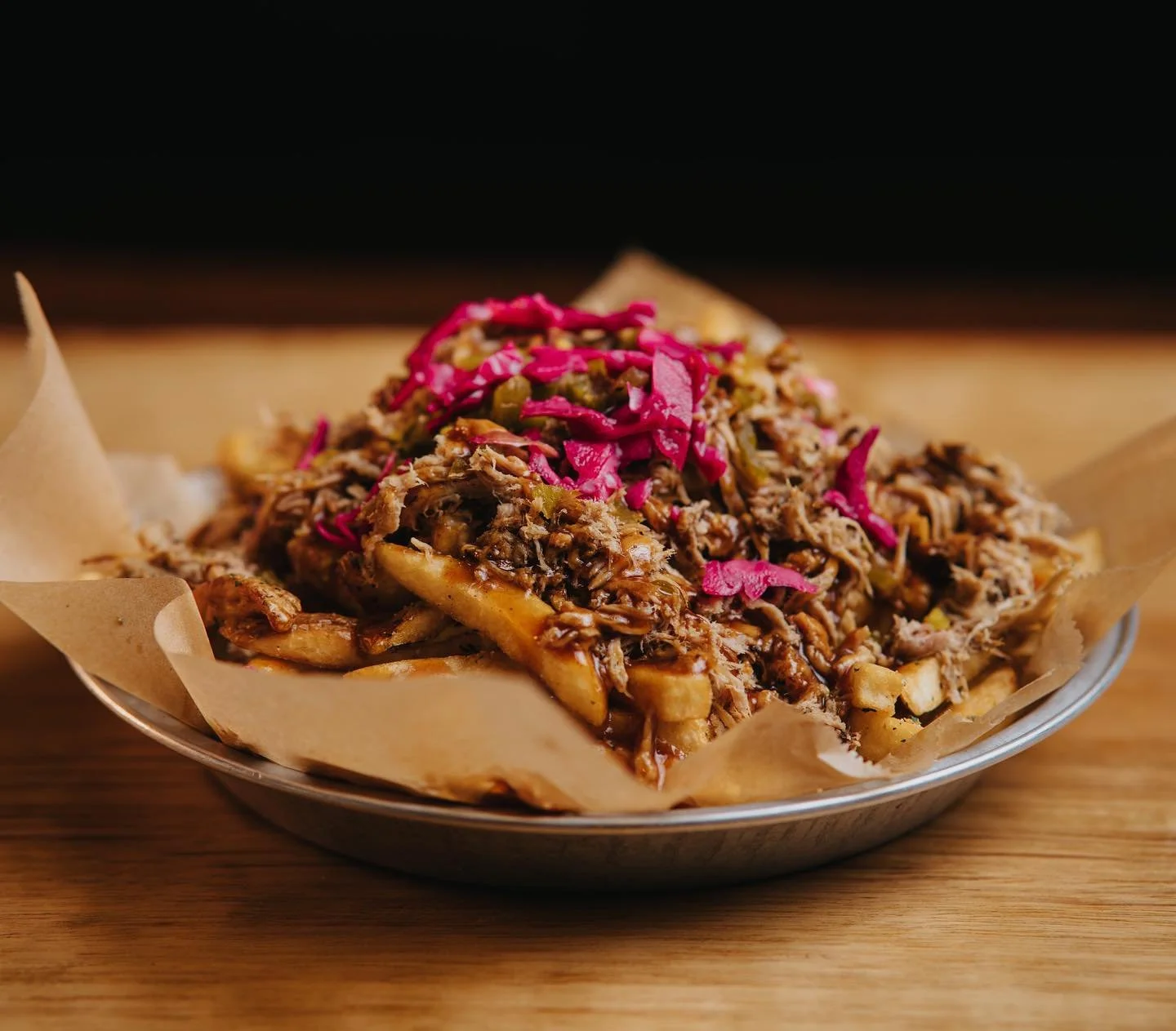 Plate of pulled pork with barbecue sauce, fries, and topped with pickled red cabbage.