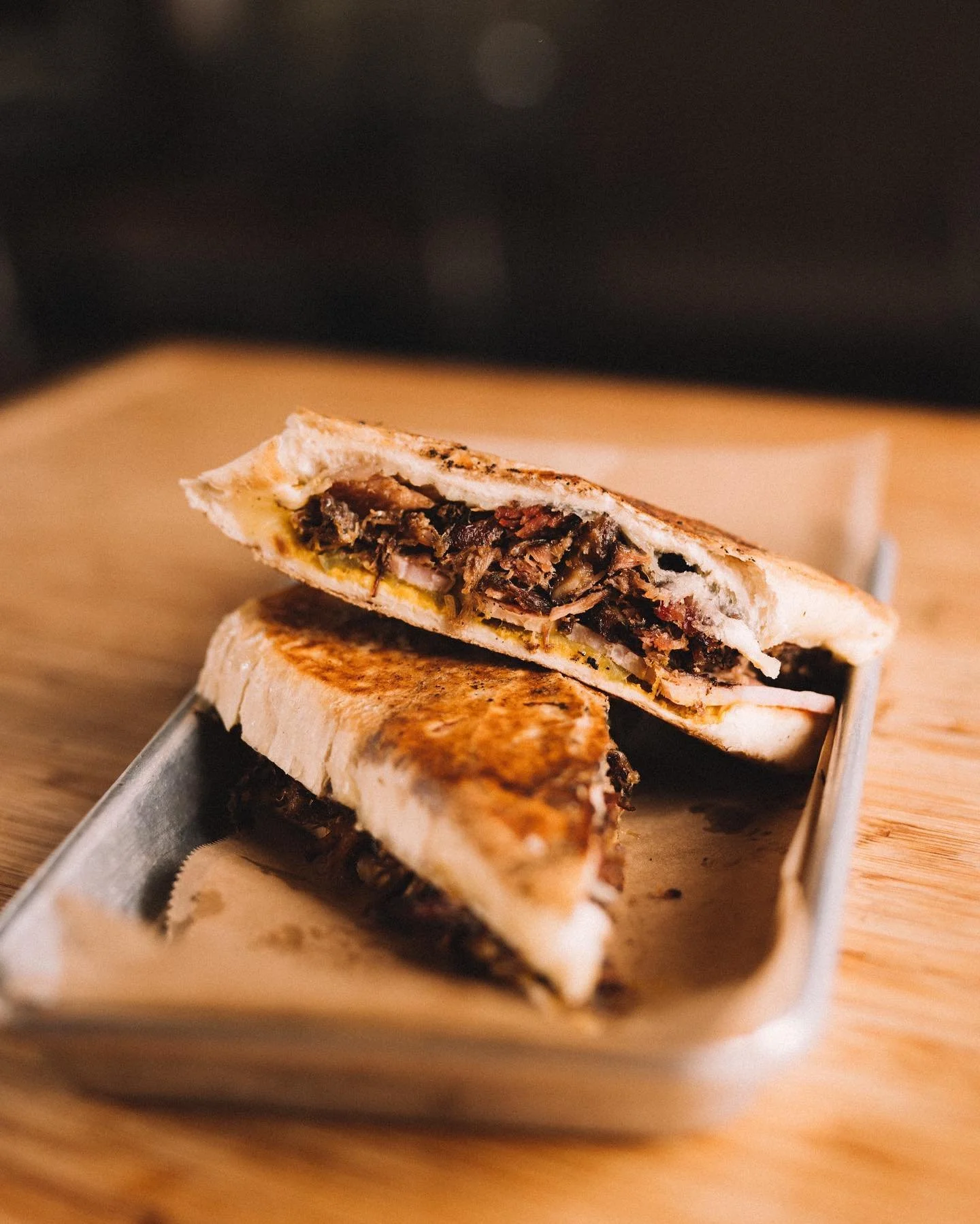 Cross-section of a pulled pork grilled cheese on a metal tray, on a wooden surface.