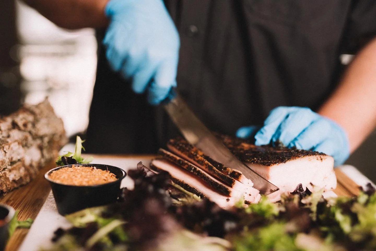 A chef slicing cooked meat on a wooden cutting board, with various sides like salad and sauces nearby.