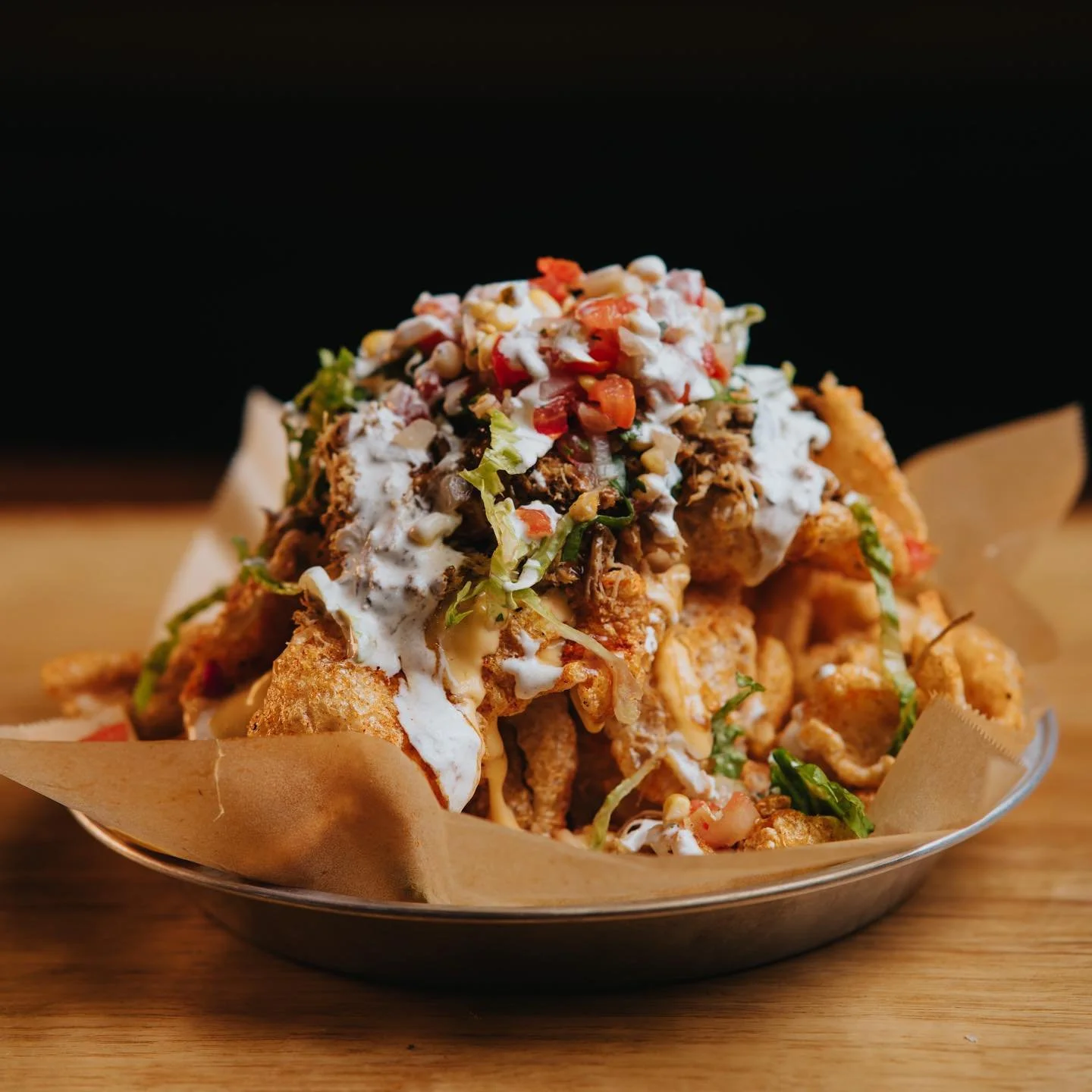 Loaded nachos with shredded cheese, sour cream, chopped tomatoes, lettuce, and chopped onions in a bowl on a wooden table