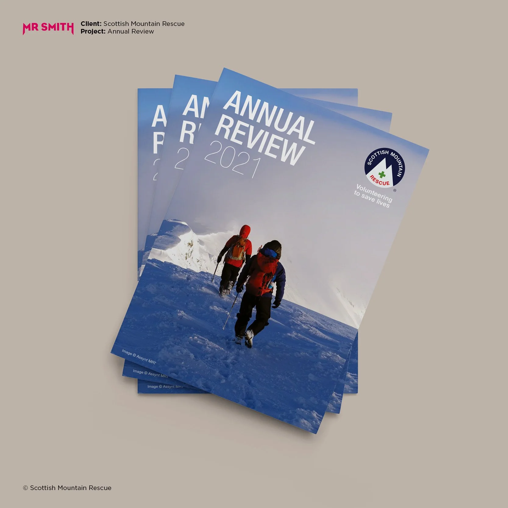 Multiple copies of a Scottish Mountain Rescue annual review pamphlet with a cover photo of three hikers ascending a snowy mountain.