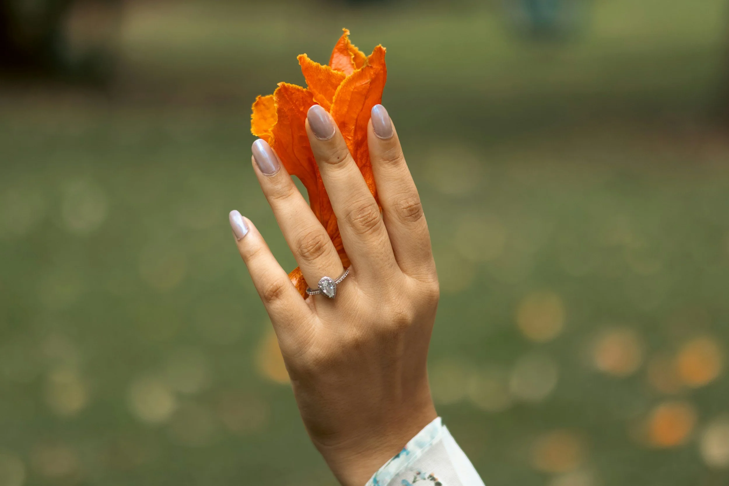 Close-up of a hand wearing an engagement ring, held in a partner's hand outdoors