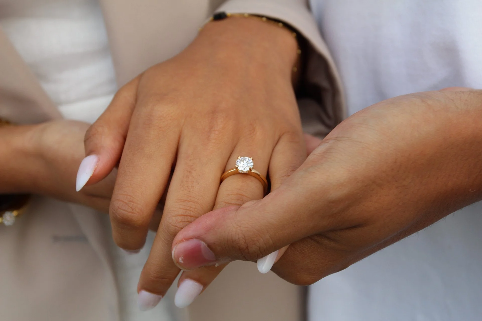 A hand with an engagement ring resting in a partner's hand