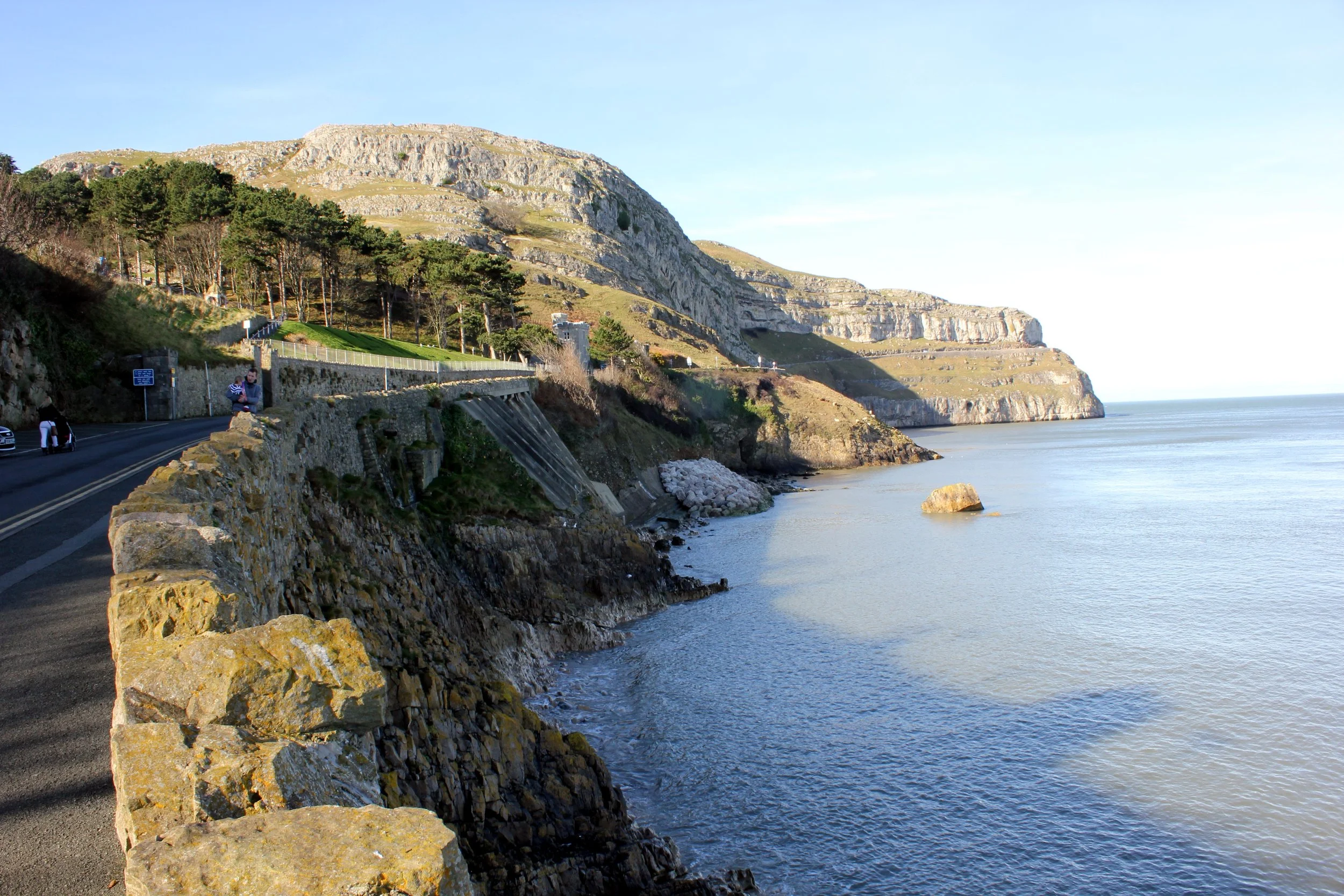 The limestone cliffs of the Great Orme rising above the calm sea beside Marine Drive in Llandudno