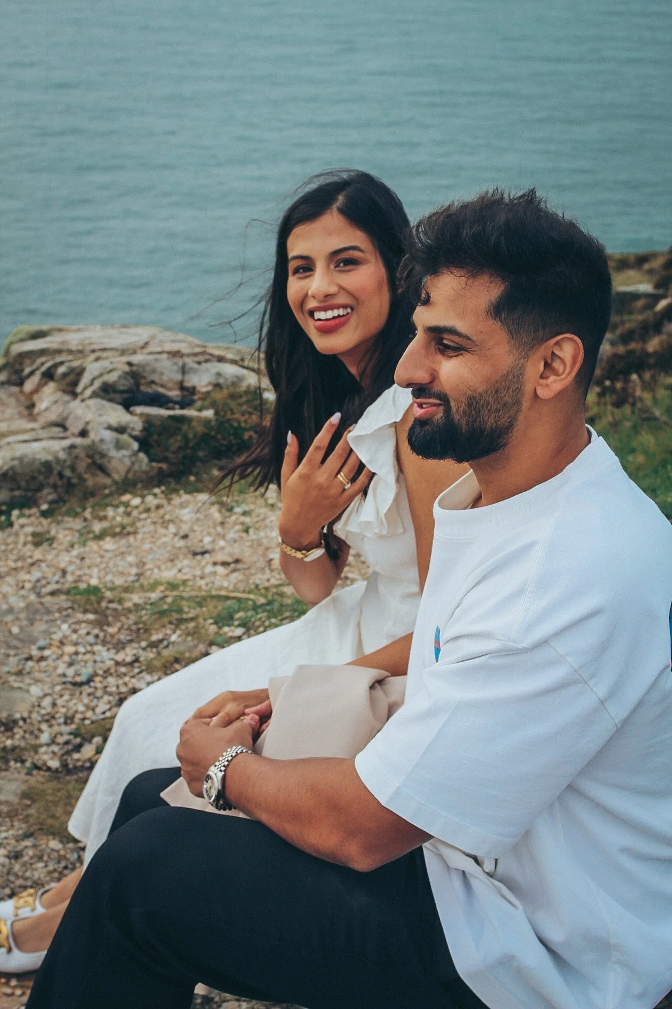A smiling couple sitting together on rocks by the sea