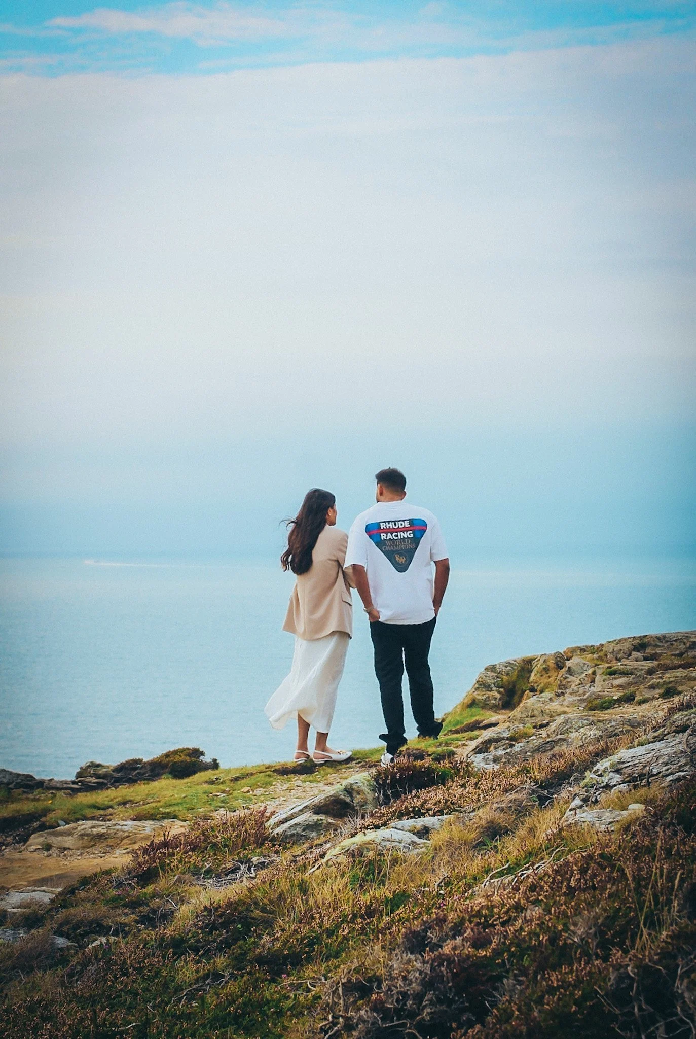A couple standing together on a grassy clifftop above the sea