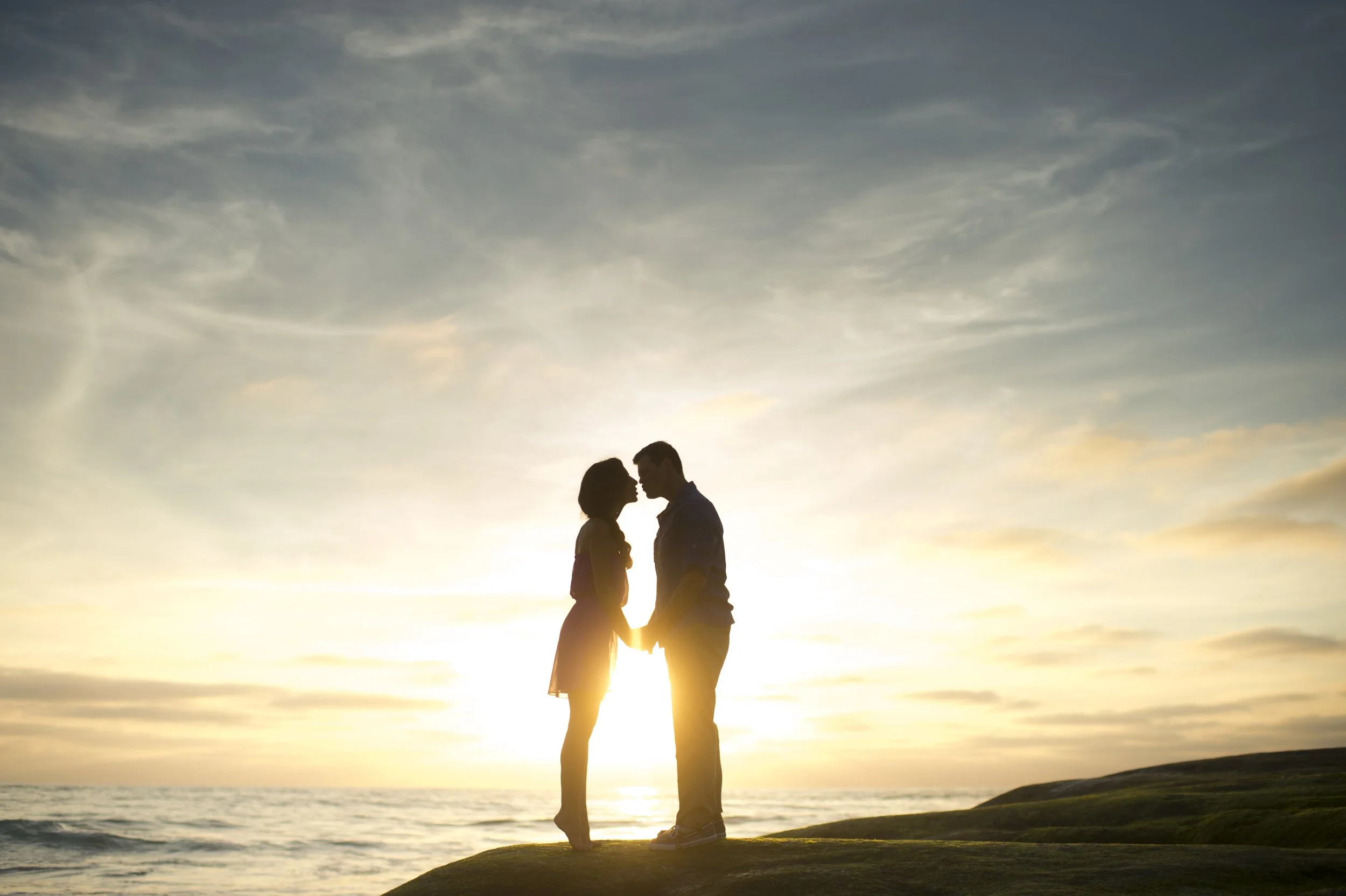 A couple kissing, silhouetted against a soft sunset sky
