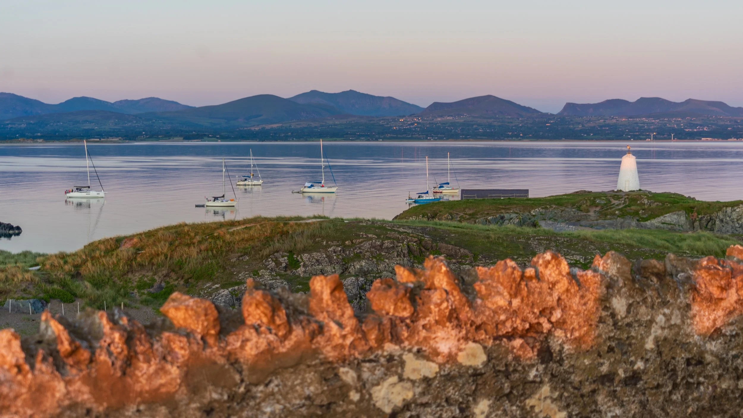 Boats at anchor off Llanddwyn Island, with the small white Twr Bach beacon and the mountains behind