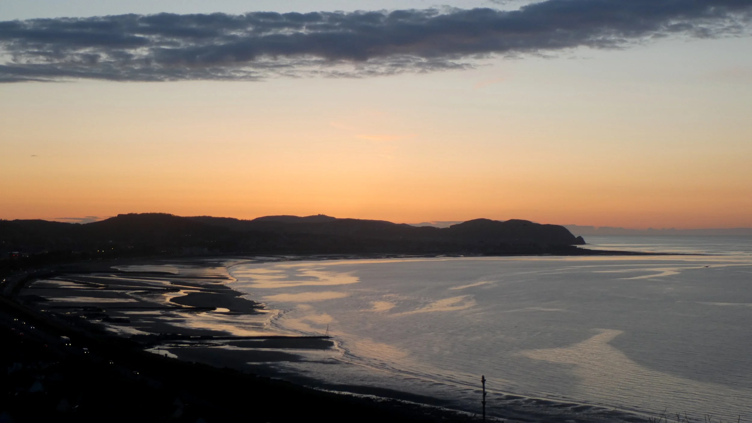 The sun setting in orange and gold over the sands and sea at Colwyn Bay