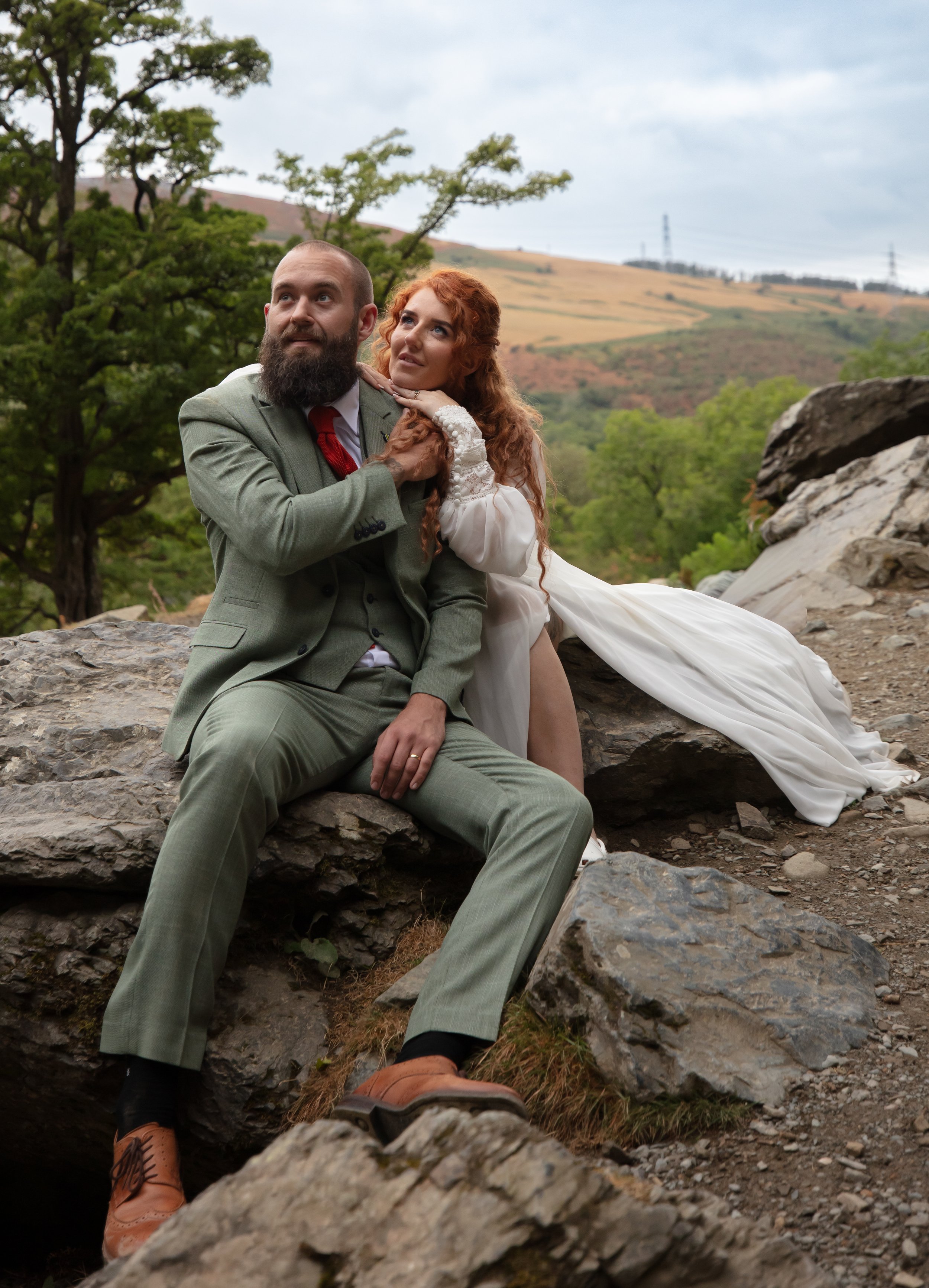 A couple sitting on a rock, embracing, with trees and hills behind