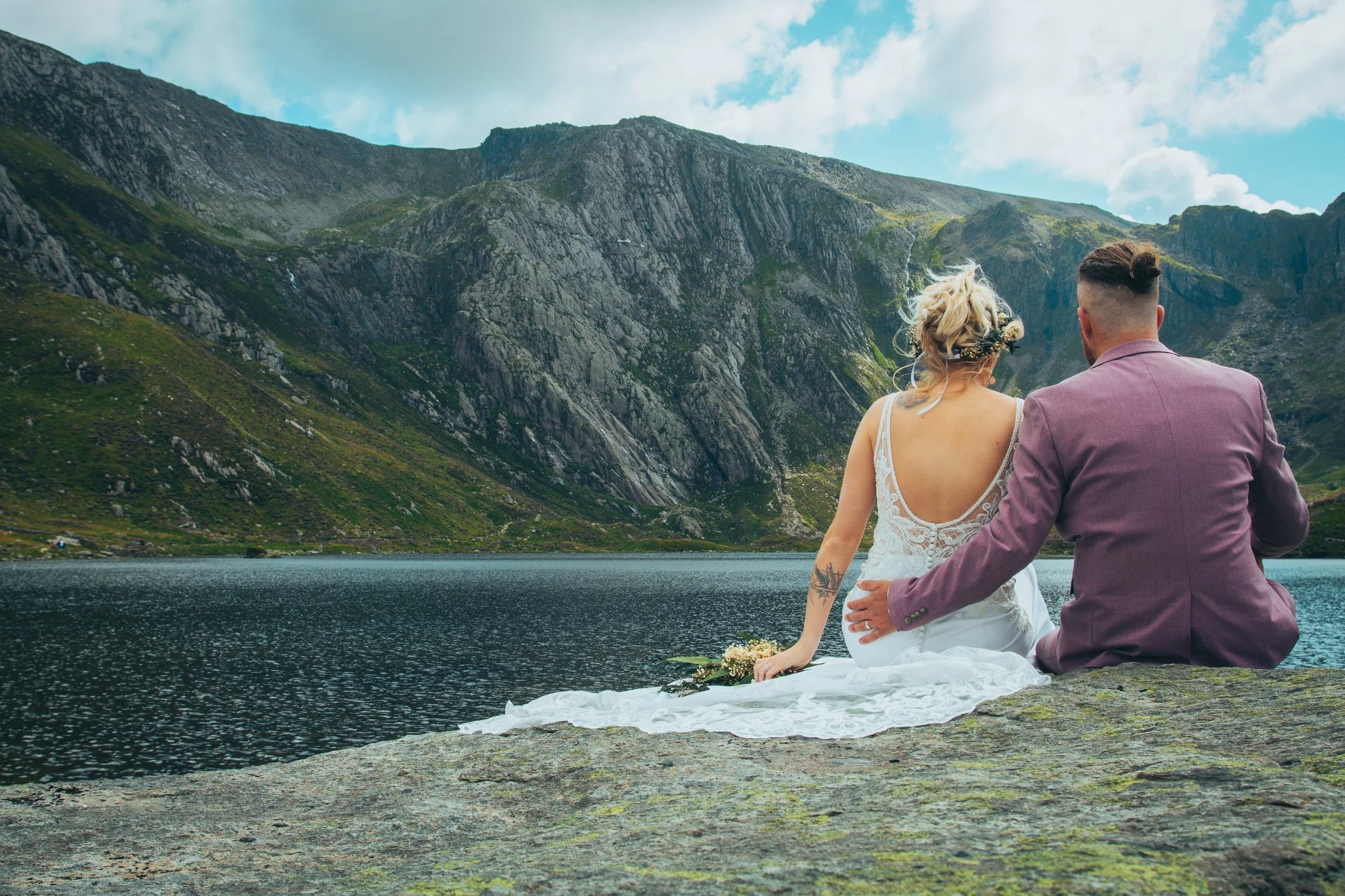 A couple sitting together on a rock beside a mountain lake