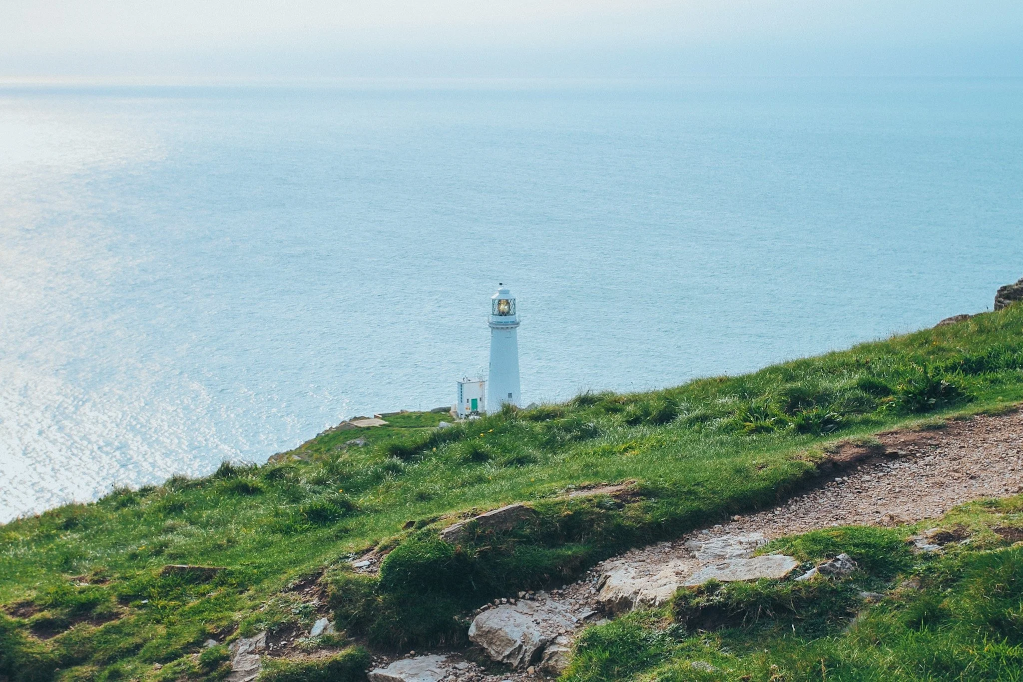 A white lighthouse on a green clifftop above the sea