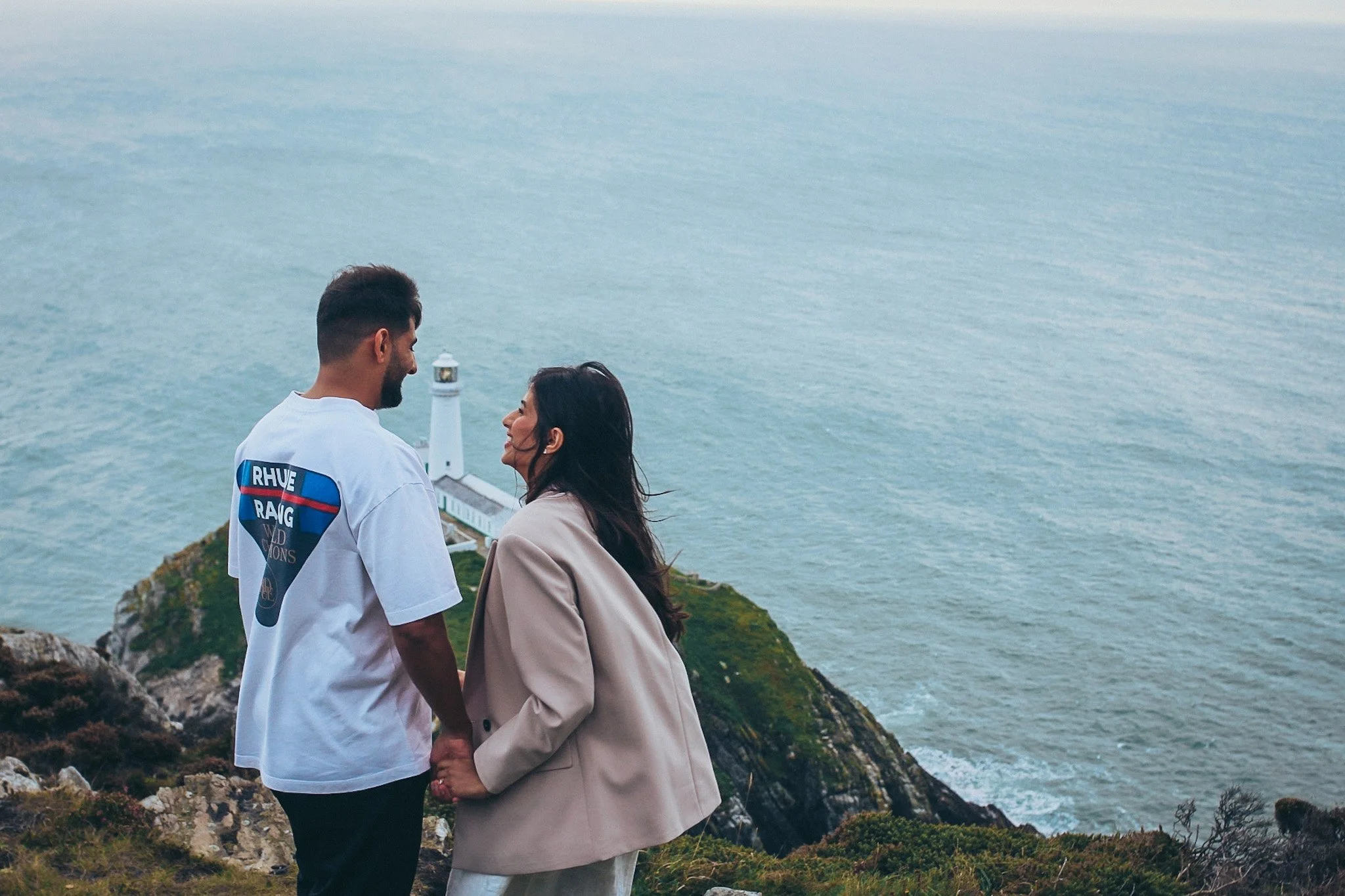 A couple holding hands on a clifftop above the sea
