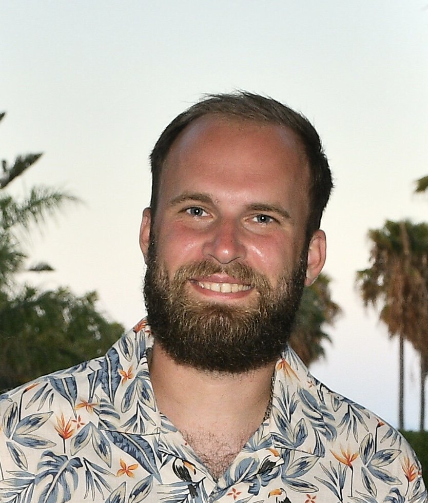 Portrait of Leon Bagnall smiling, with palm trees behind him