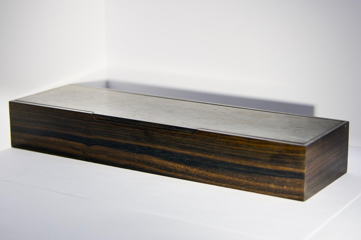 A rectangular wooden box with a slide top lid, resting on a white surface.