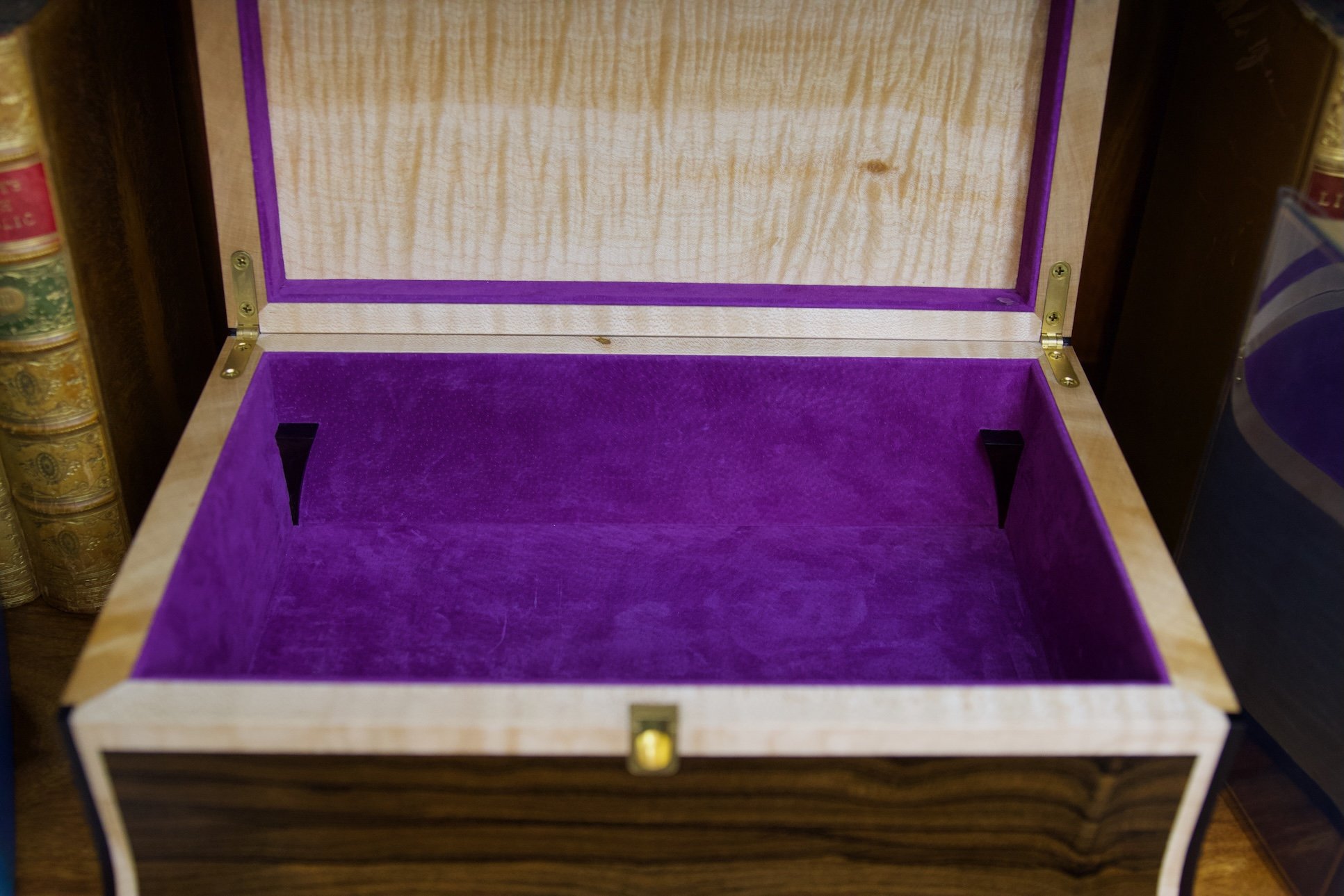 Open wooden jewelry box with purple velvet interior and a hinged lid.