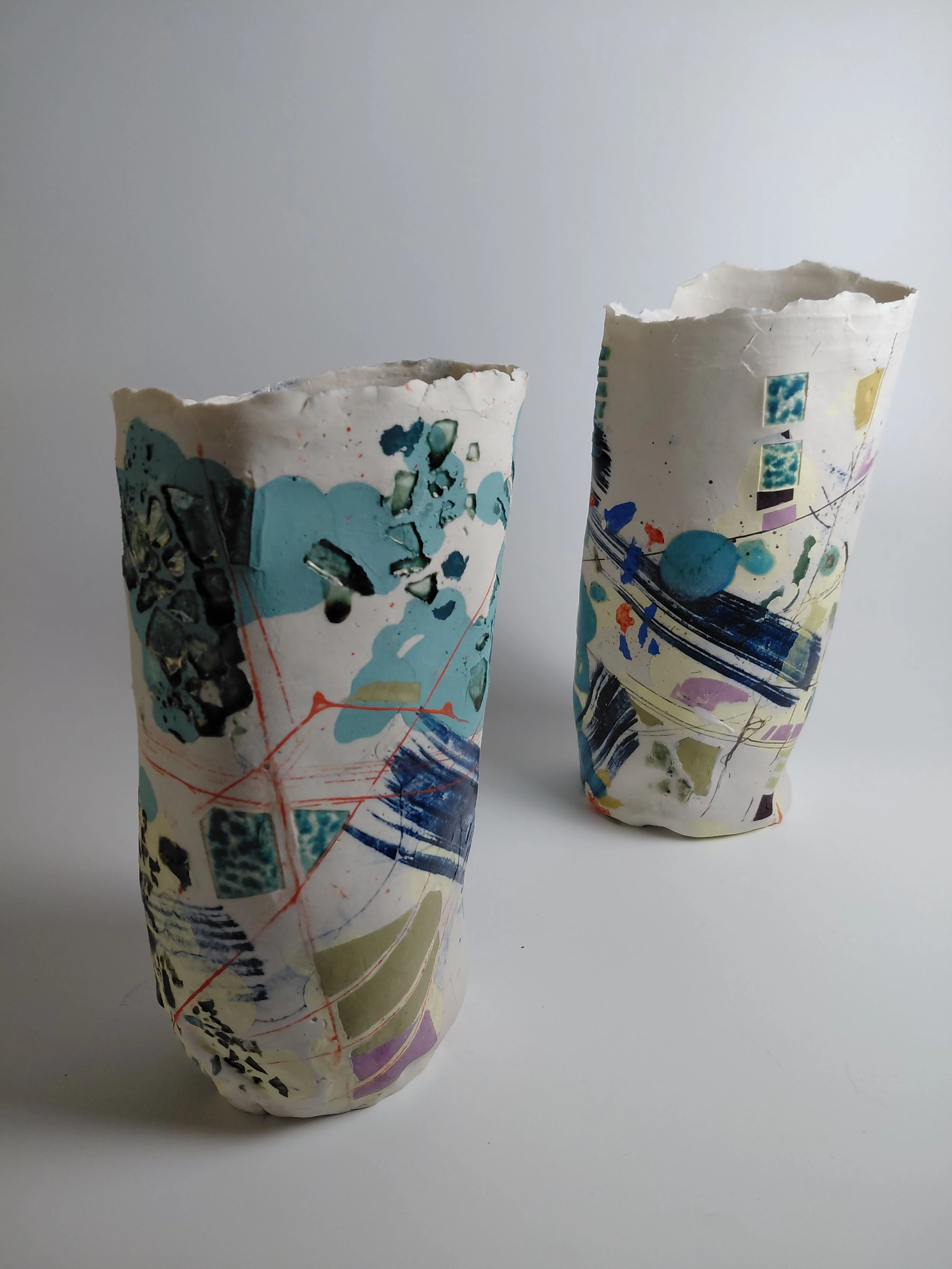 Two crumpled paper cups with colorful abstract patterns on a white surface against a light gray background.
